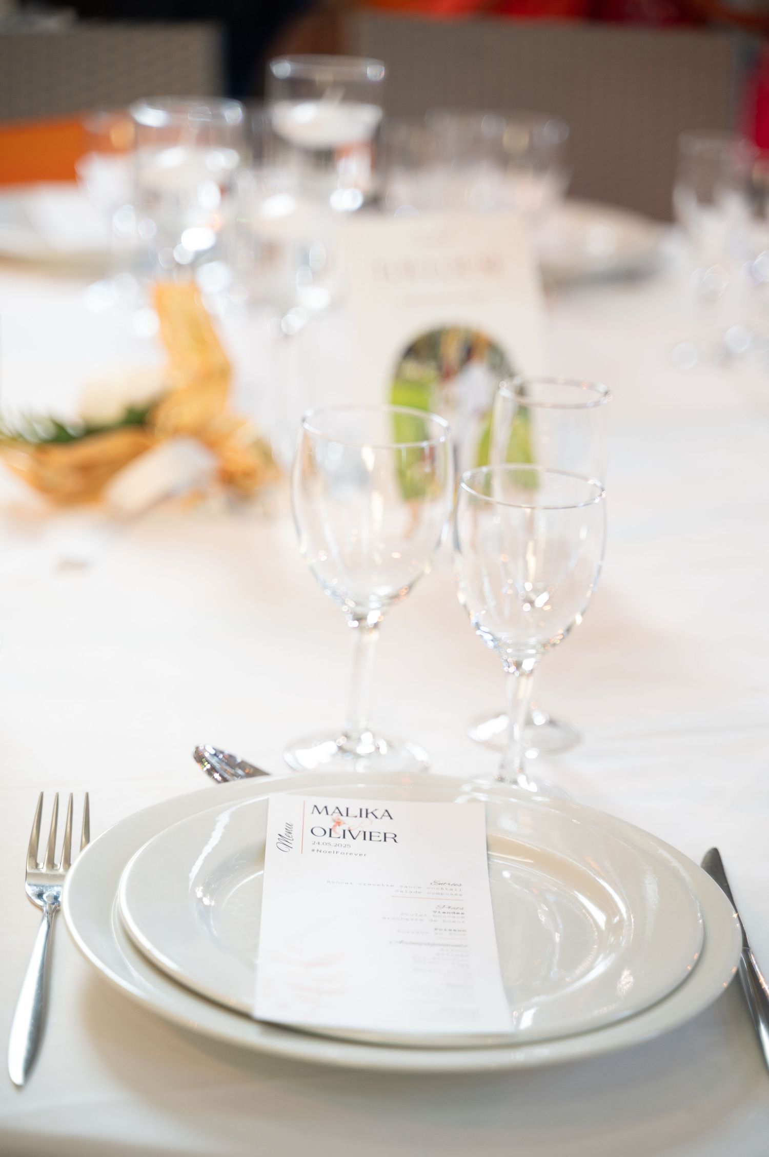 Formal wedding table setting featuring Malika and Olivier menu card, white plates, and stemmed glasses.