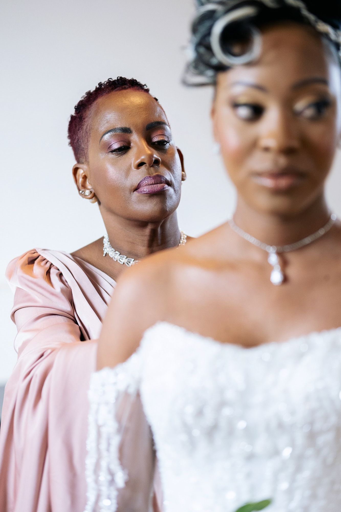 Woman in pink dress adjusting the shoulder of a bride in a white strapless wedding gown.
