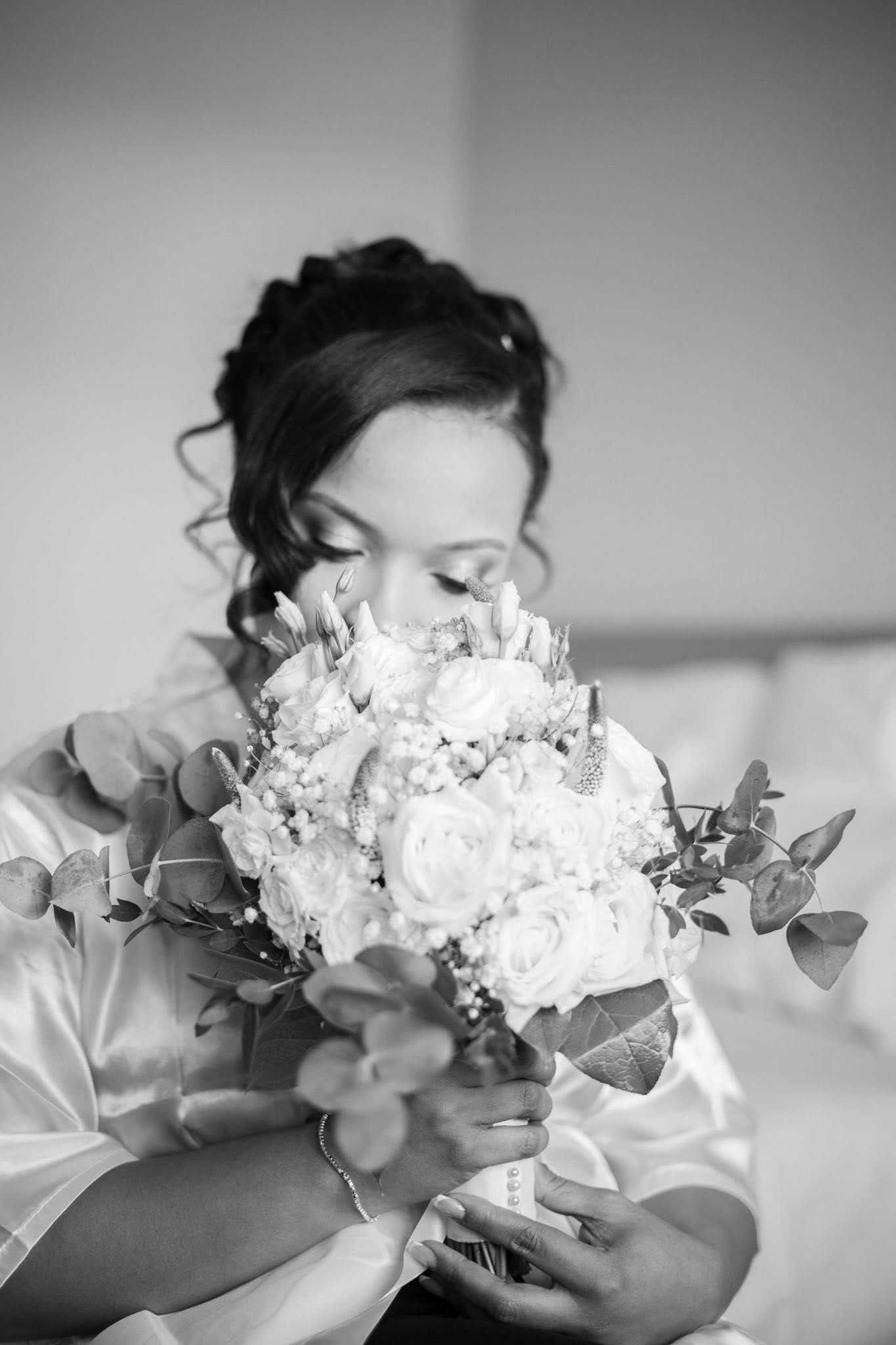Black and white photo of a bride smelling a bouquet of roses and eucalyptus in a robe.