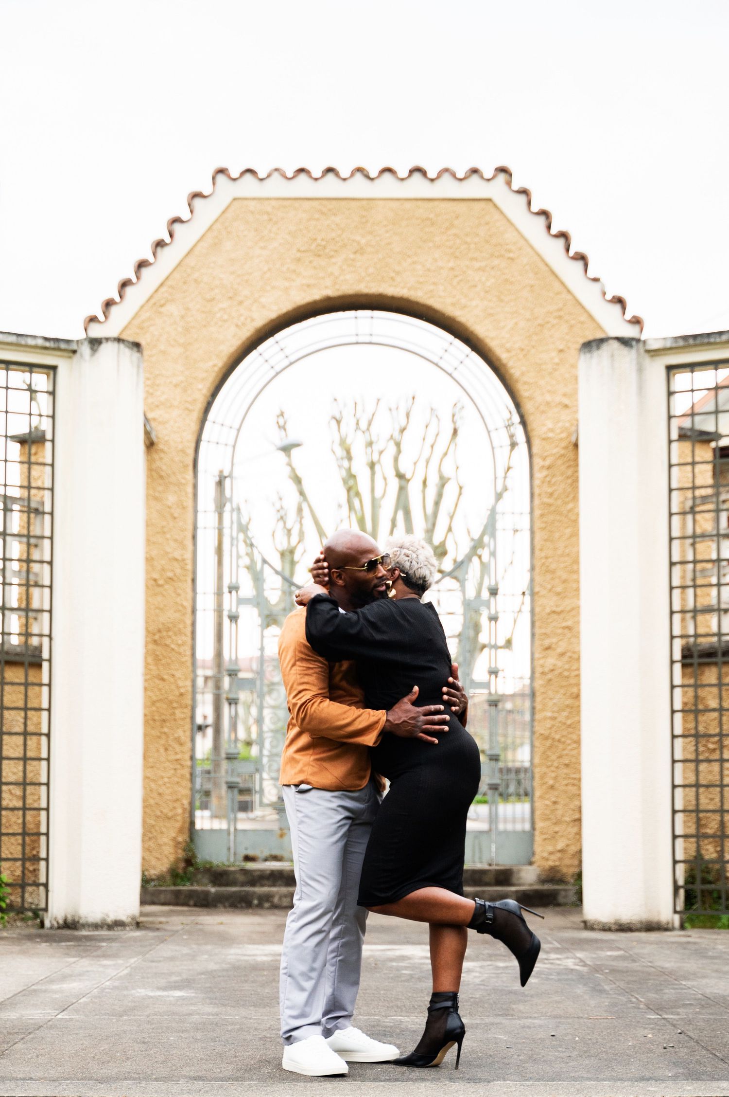 Black couple hugging under an arched gateway in an outdoor courtyard setting.