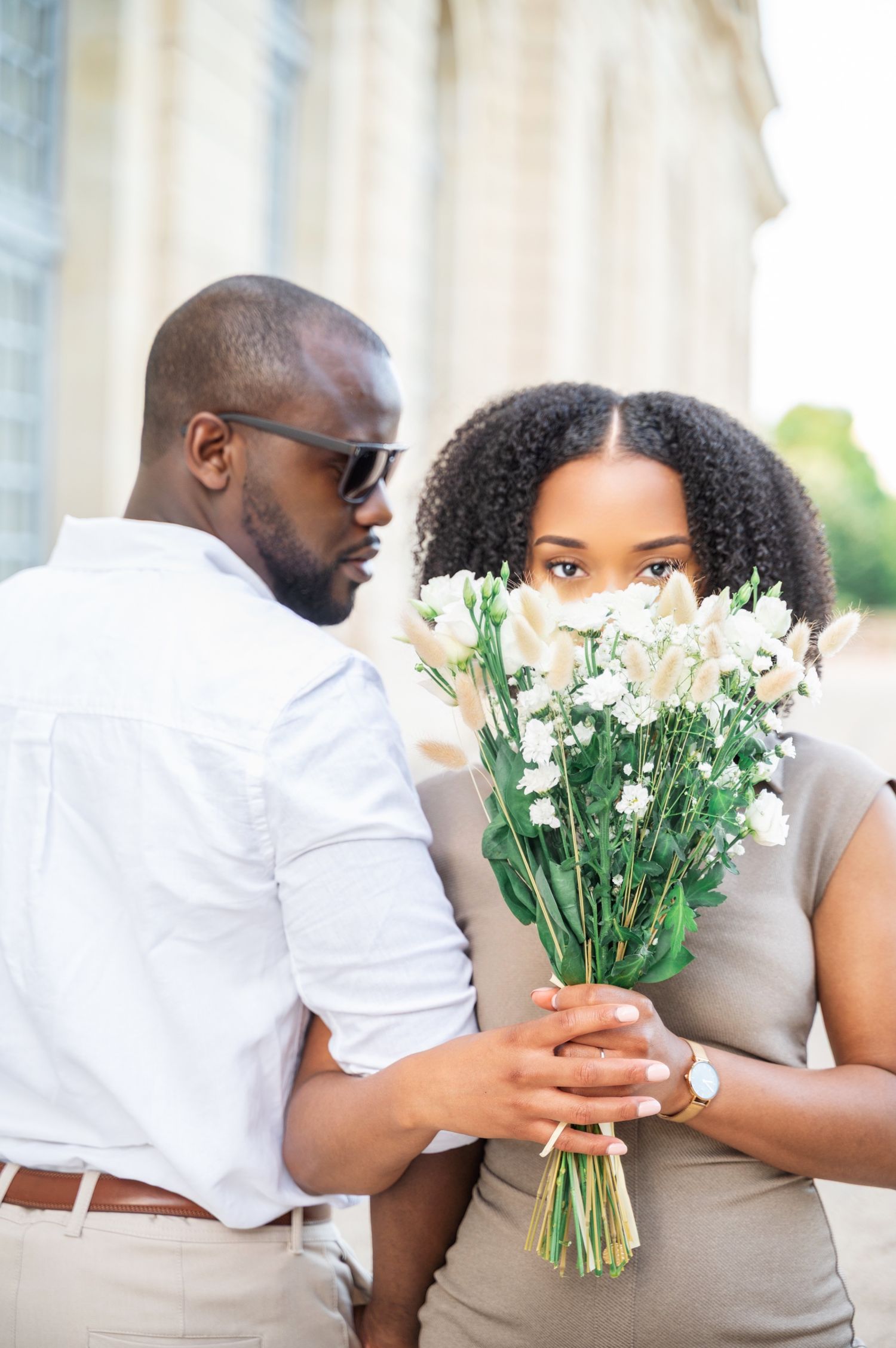 Man in white shirt presenting bouquet of white flowers to woman outdoors.