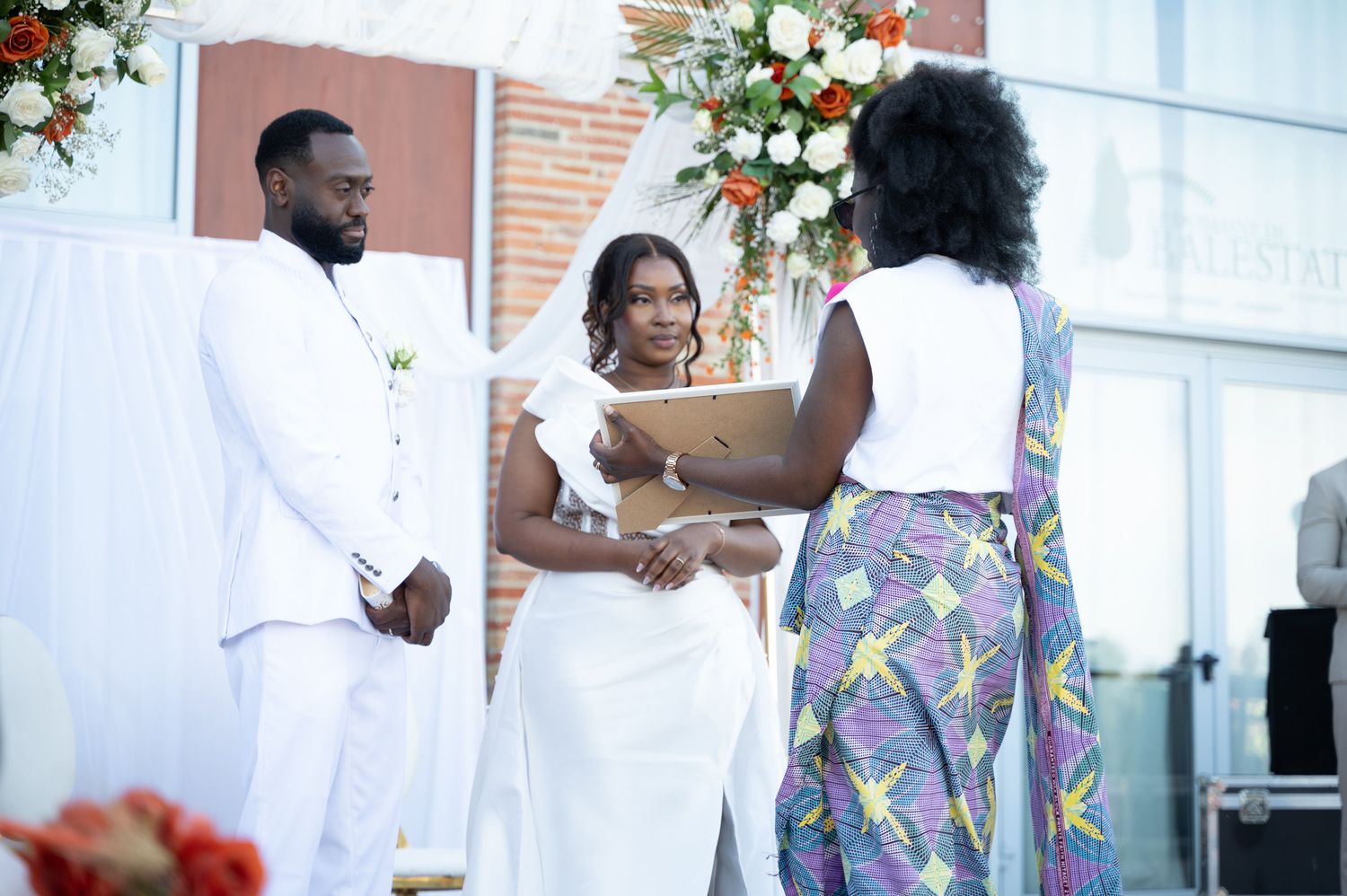 Bride and groom exchange vows as female officiant holds clipboard at outdoor wedding.