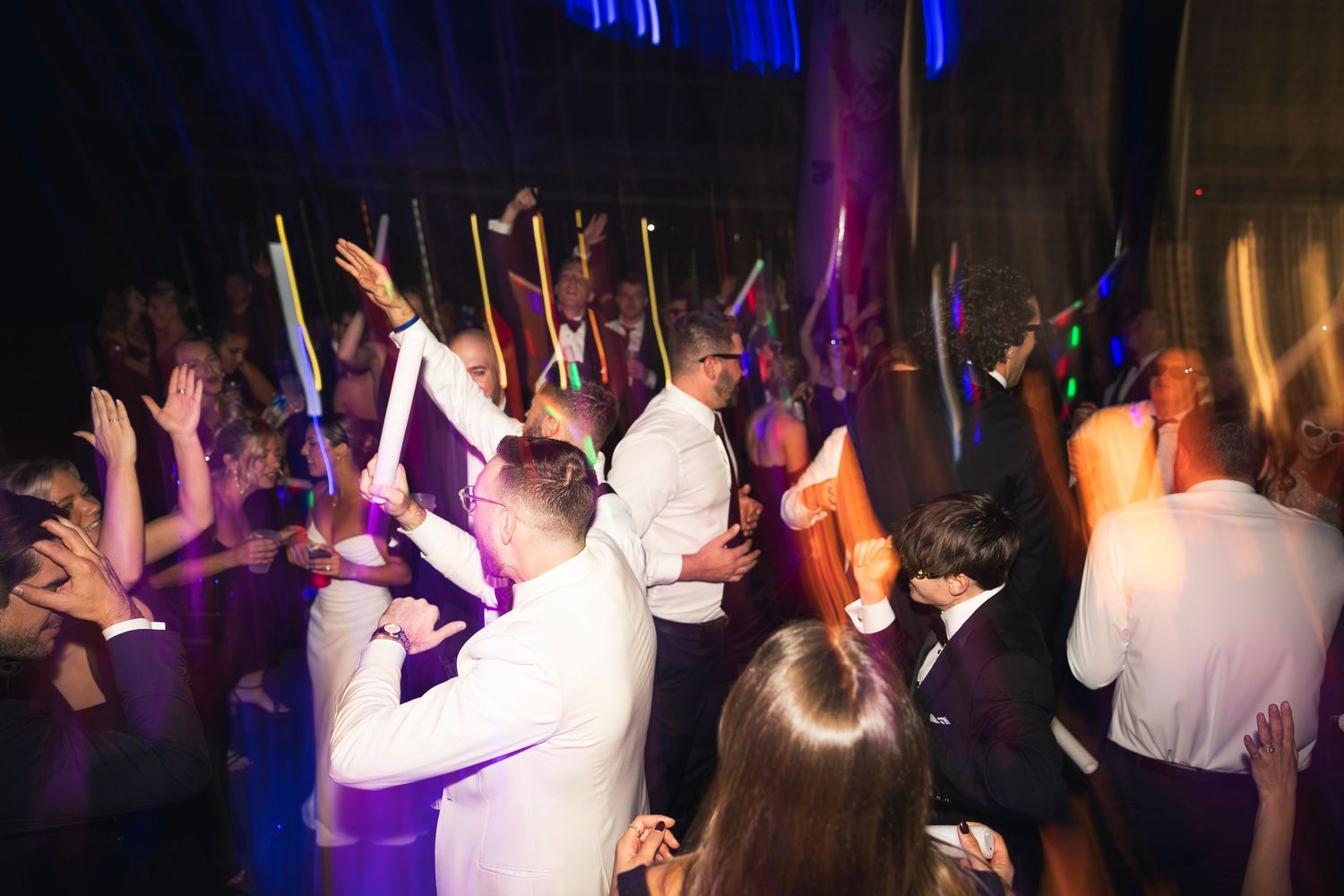 Crowded dance floor with party guests dancing under blue and purple lighting.