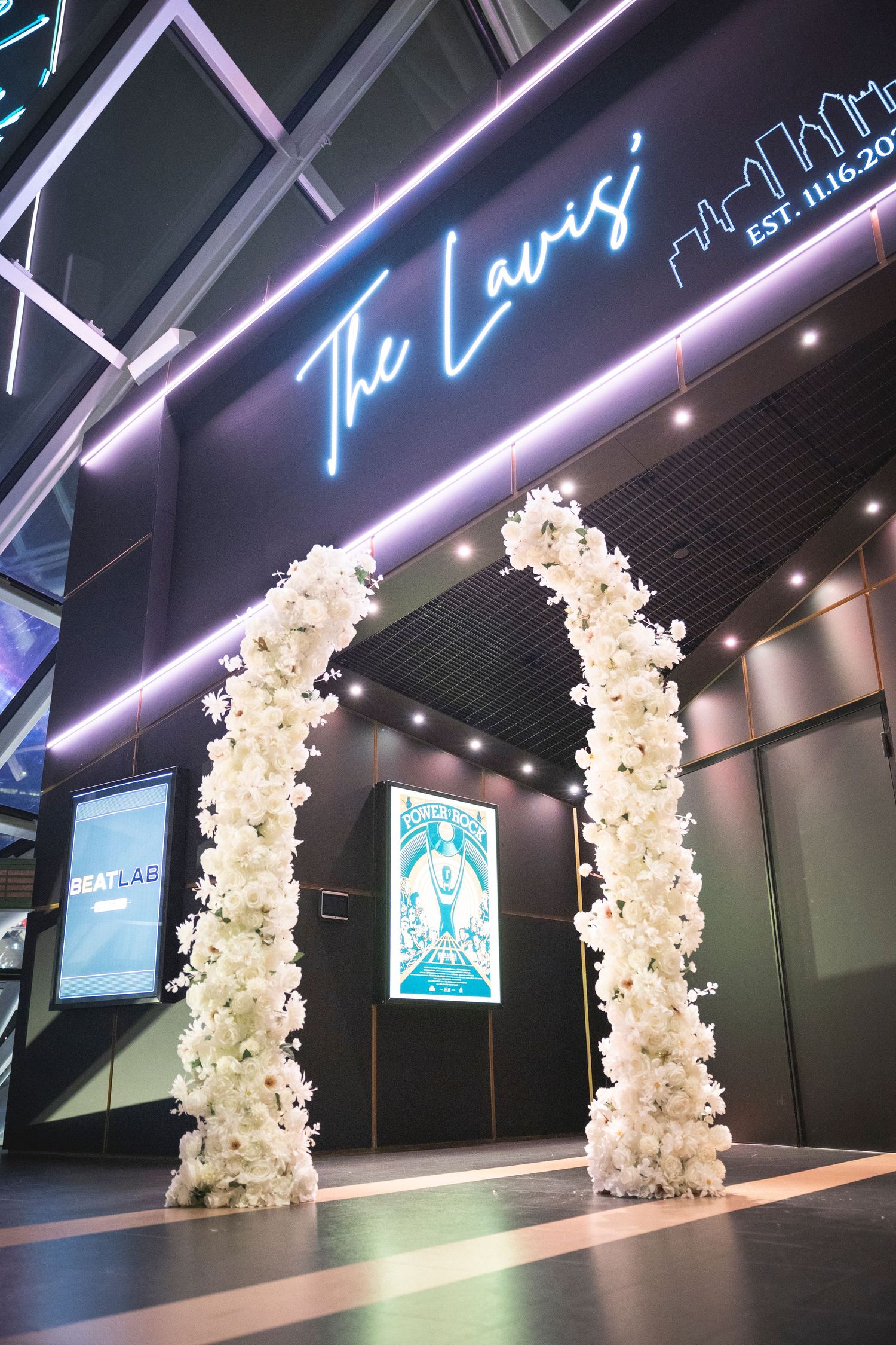 White floral arch decorations with purple neon lighting in modern event space.