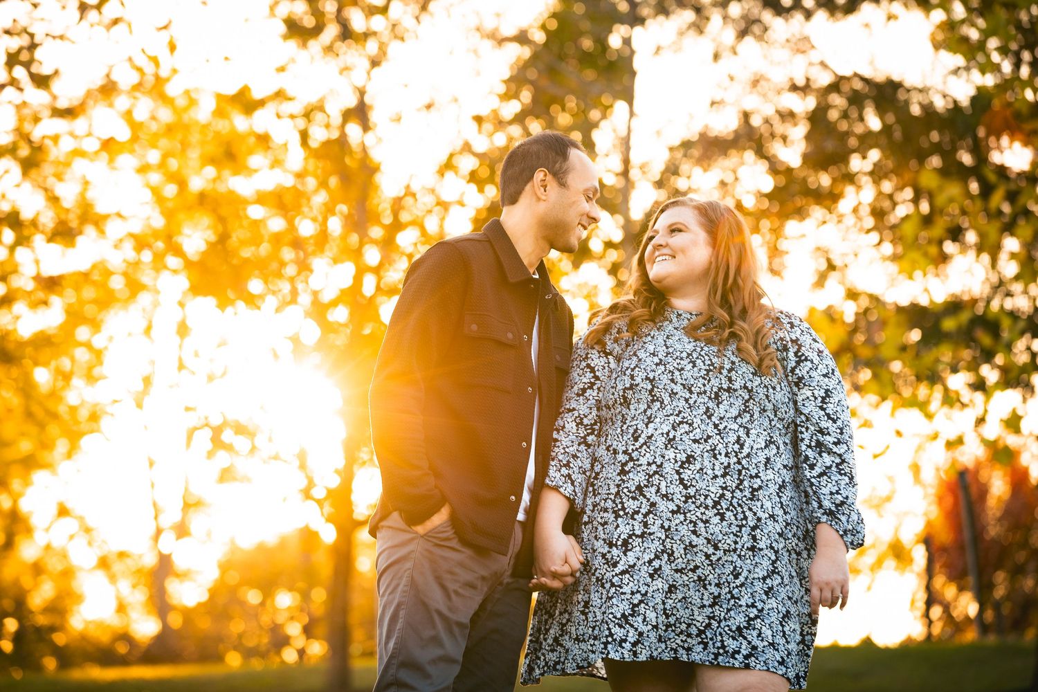 Silhouettes of a couple embracing during a golden sunset with trees in the background.