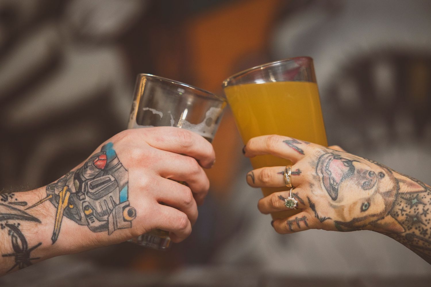 Tattooed hands holding drinks across table.