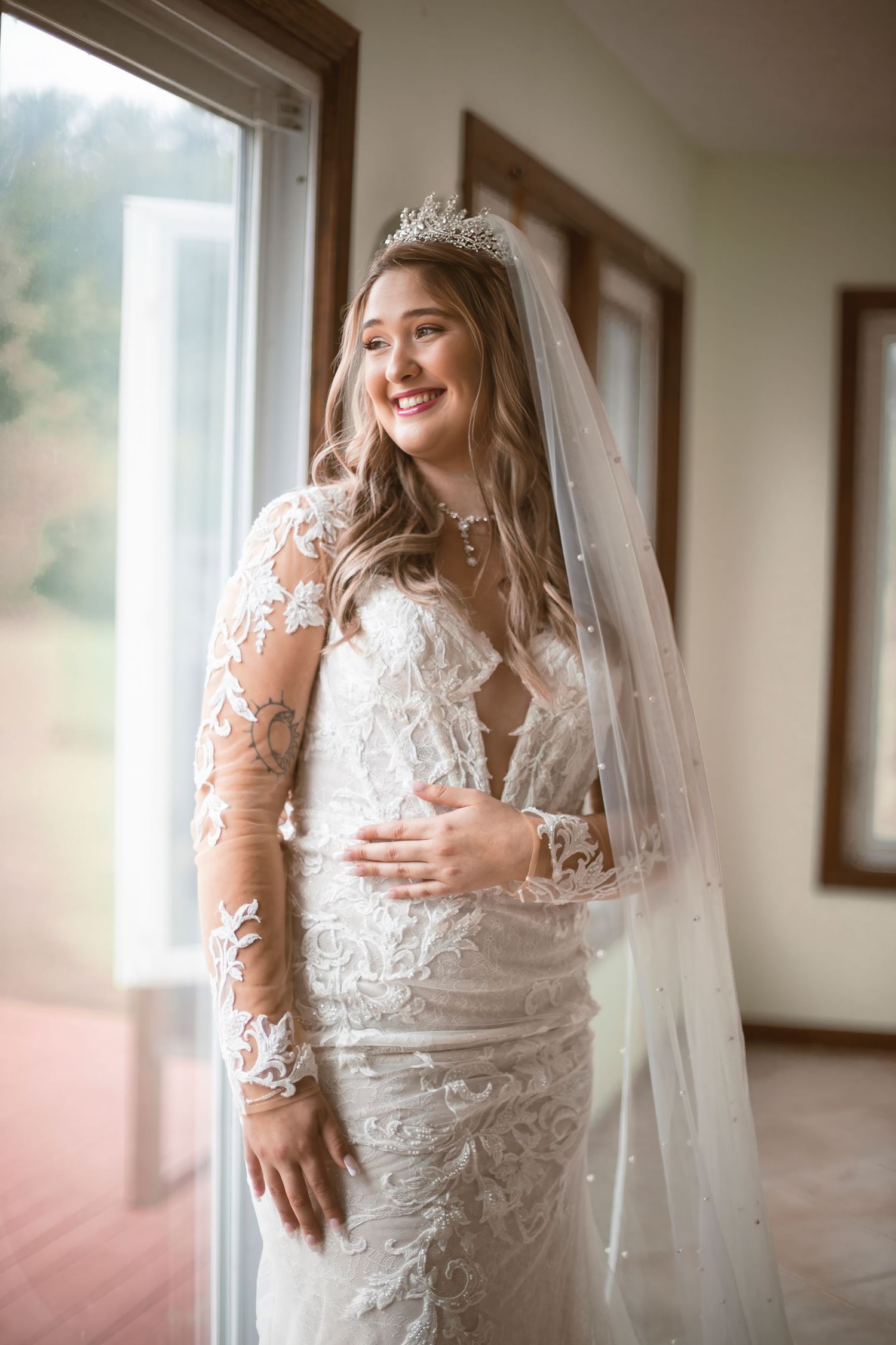Wedding dress details showing intricate lace sleeves and veil in natural window light.