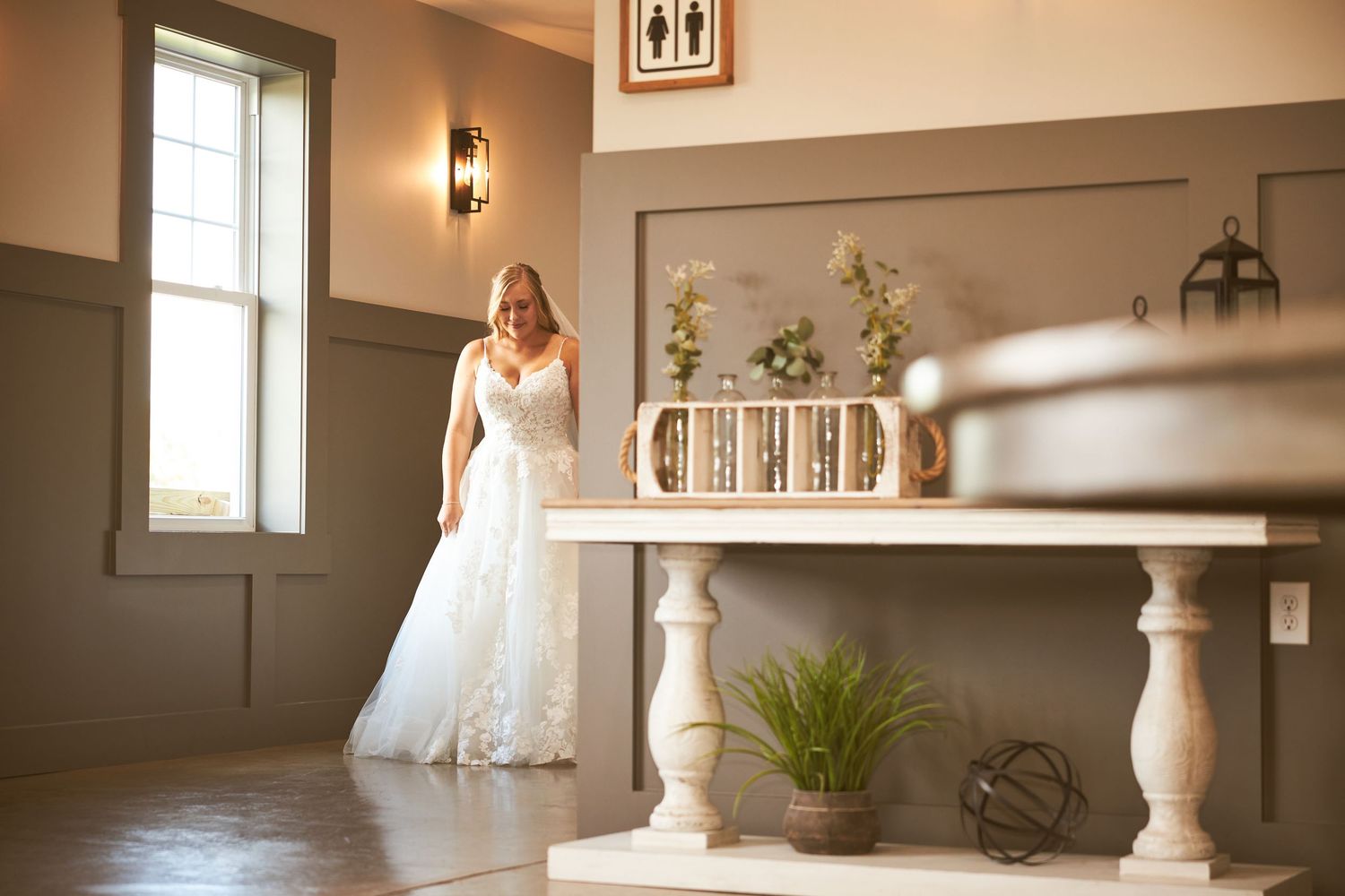 Bridal portrait in elegant white lace gown next to decorative white furniture.