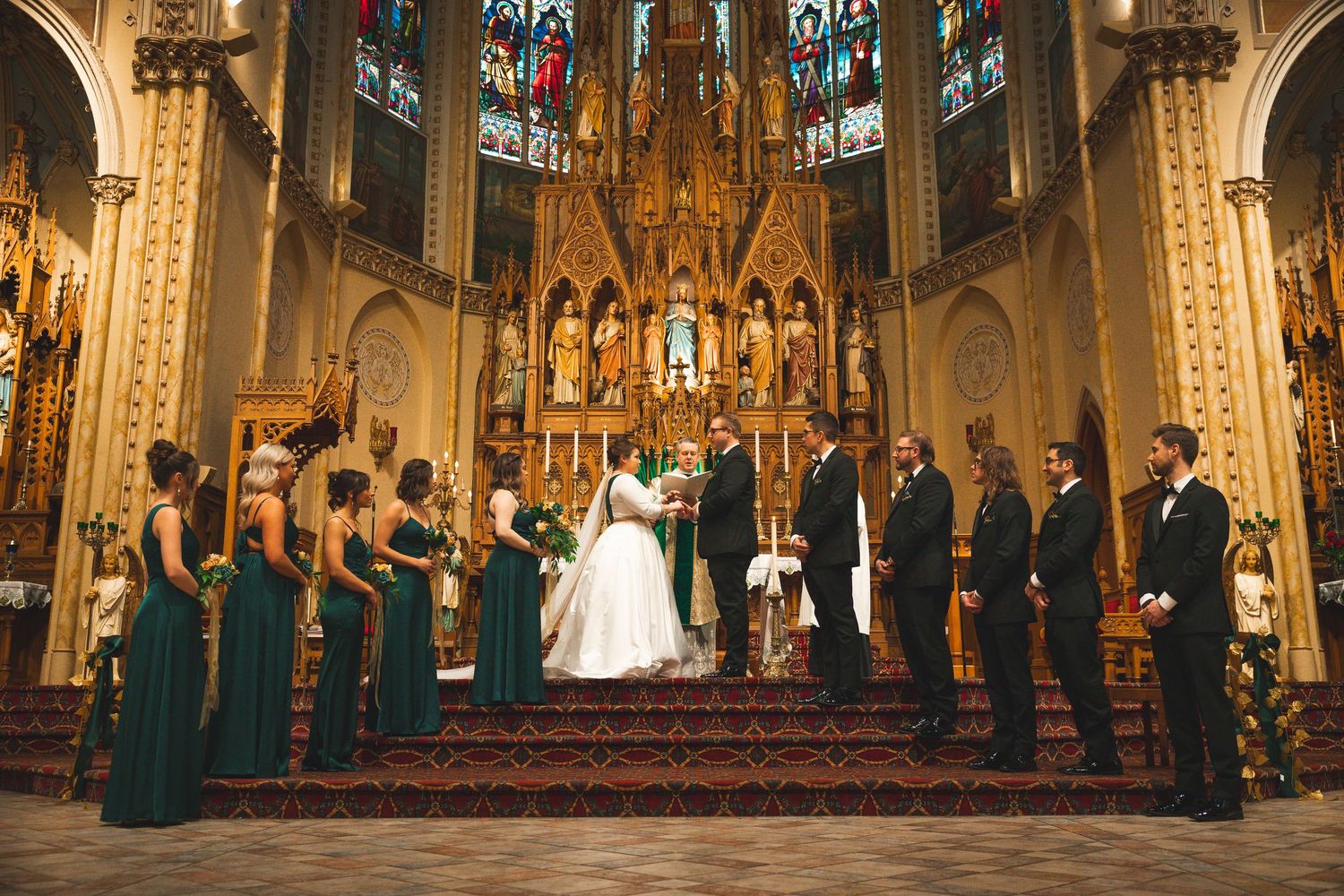 Wedding party in emerald green attire stands at the altar of a grand cathedral.