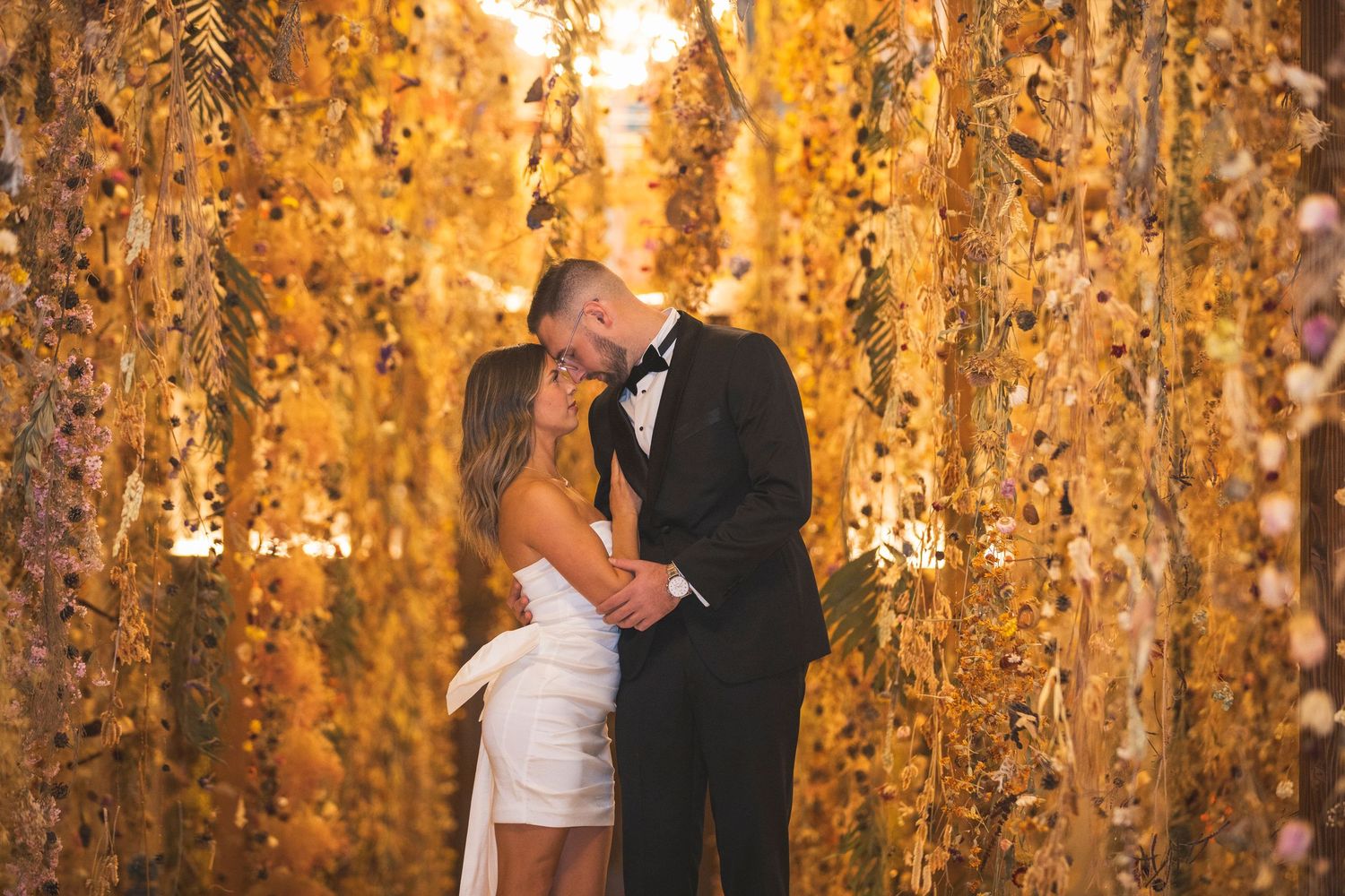 A romantic wedding kiss under cascading golden autumn leaves and warm lighting.