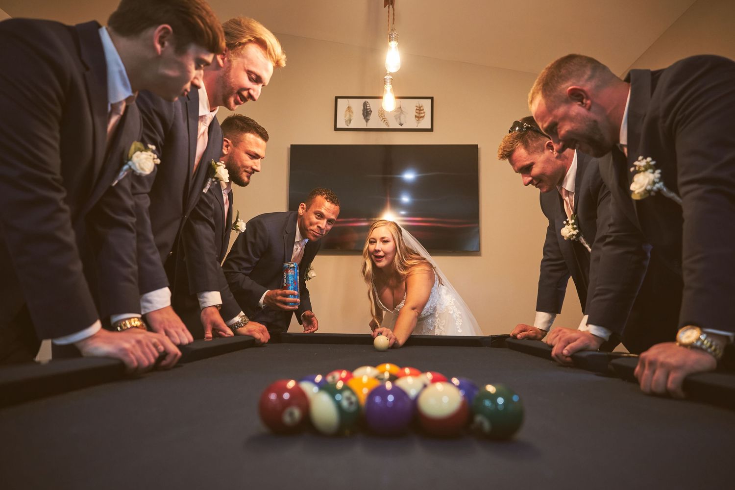 Wedding guests play pool in a dimly lit game room.