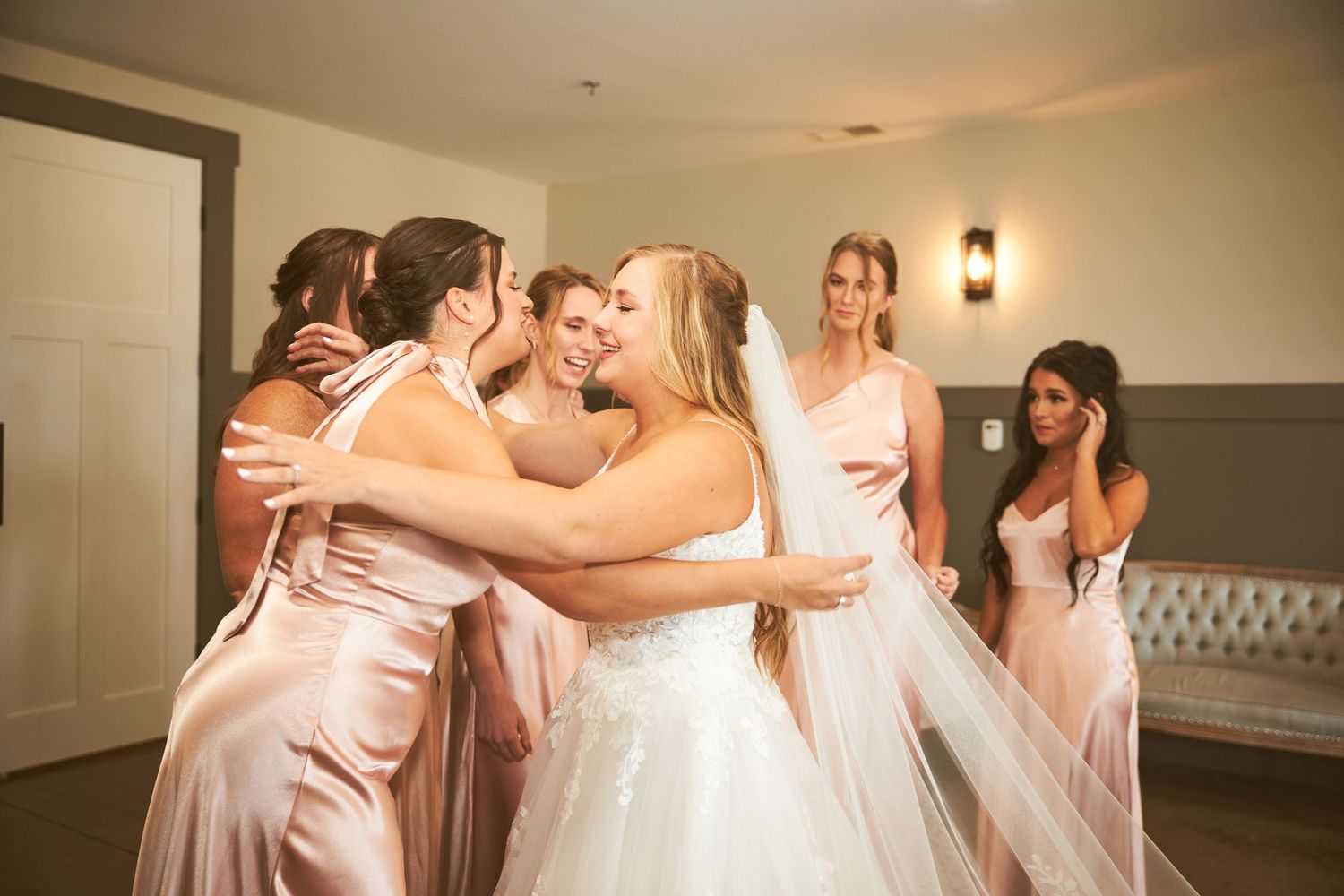 Wedding party celebrating with emotional embraces in a brightly lit venue.