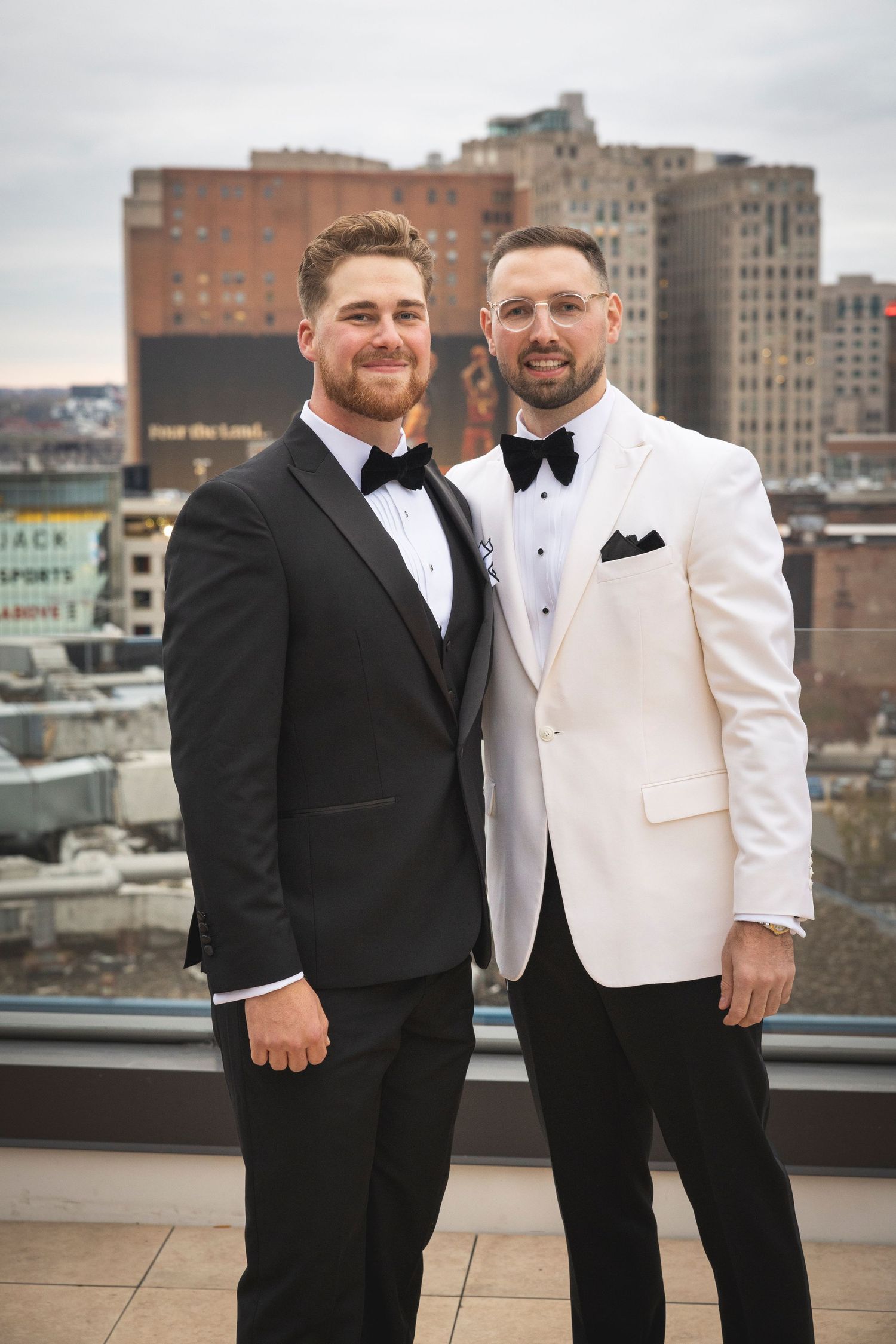 Two people in formal attire pose together on an urban rooftop terrace.