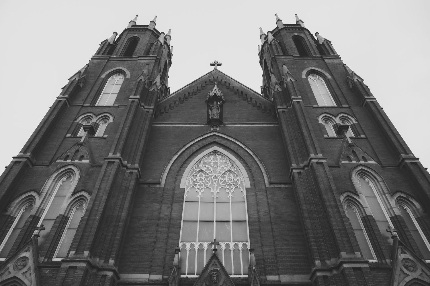 Gothic church exterior with twin spires and detailed architectural features against cloudy sky.