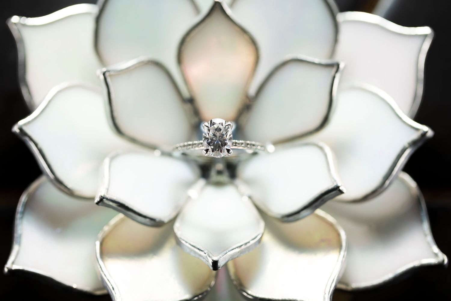 Close-up of white floral-shaped light fixture with engagement ring.