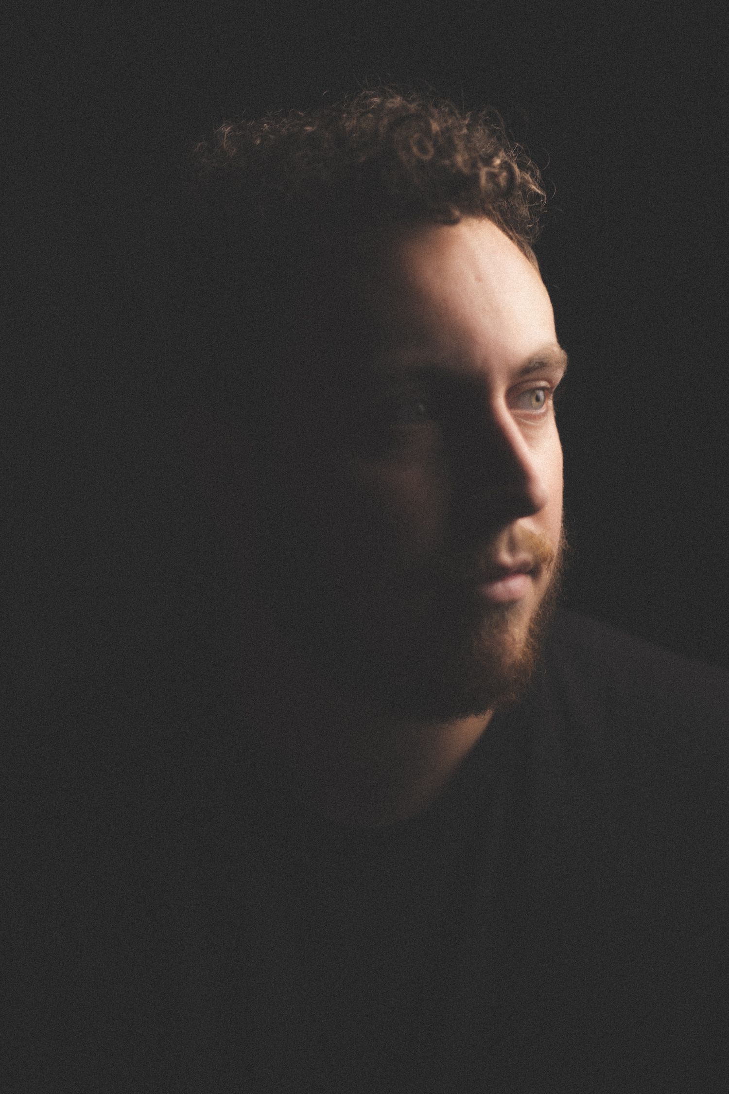 Dramatic side-lit portrait in dark setting creating mysterious shadows and highlights.