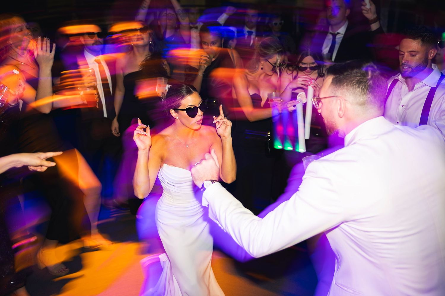 Energetic dancing and celebration at a wedding reception with colorful lighting.