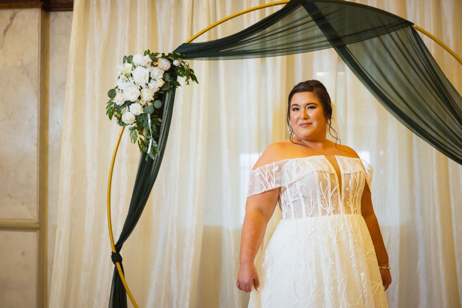 Wedding party members in mixed attire including emerald green suits smile and pose in front of elegant curtains.