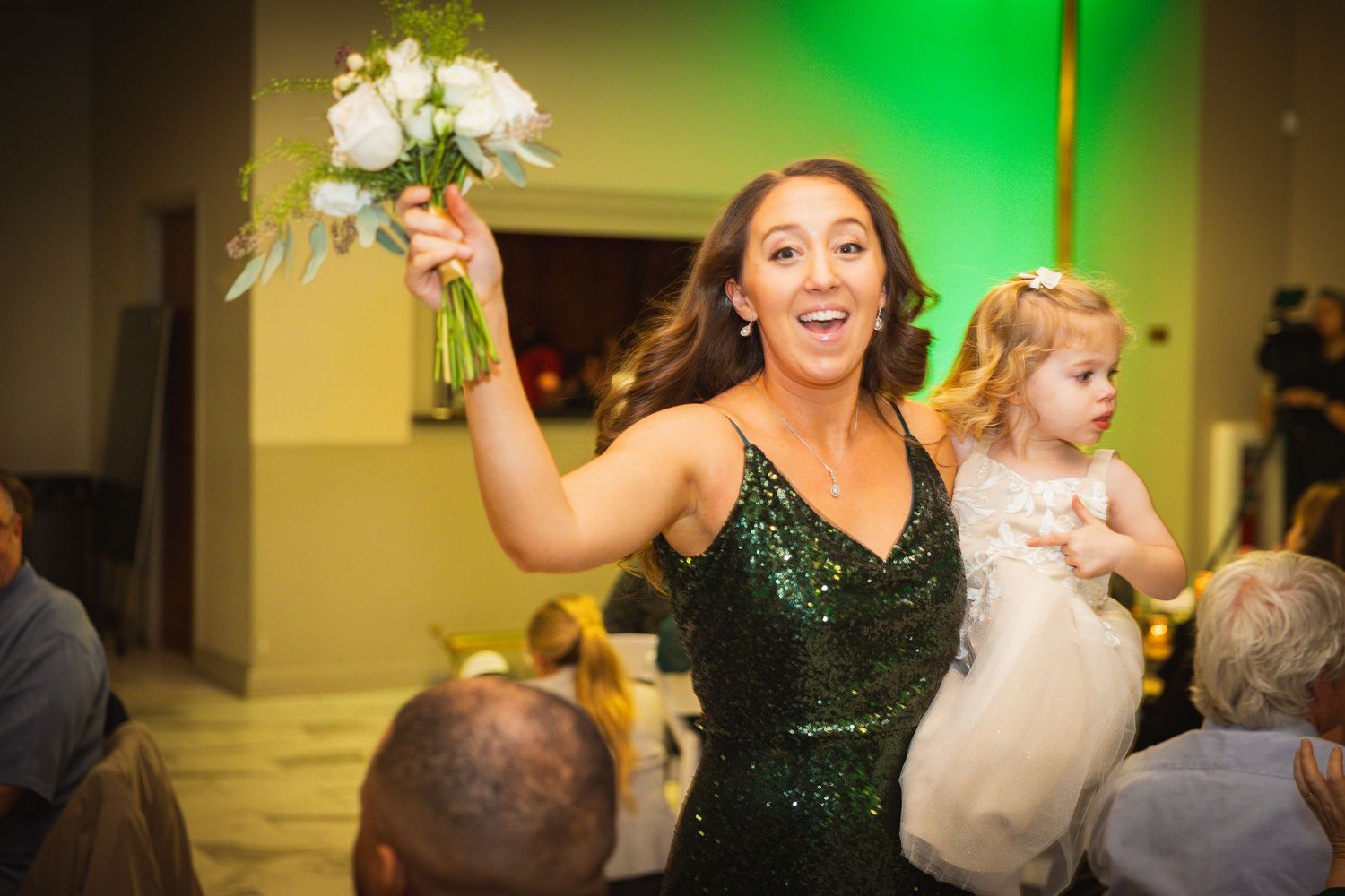 Guests enjoy a lively wedding reception as green lighting illuminates the dance floor and decorative backdrop.