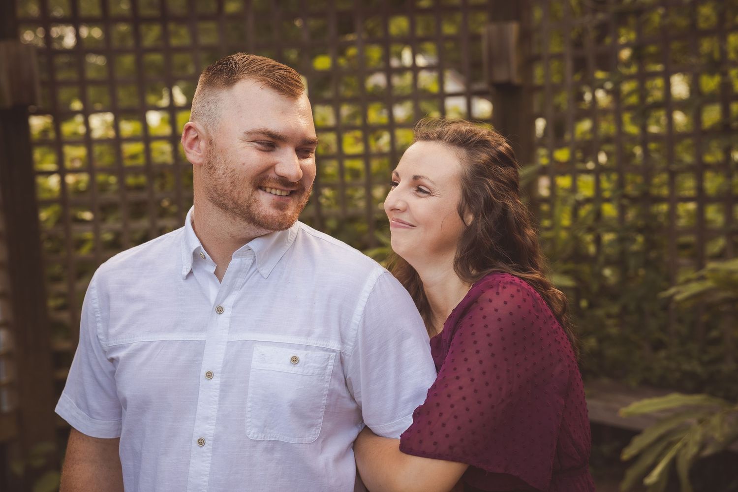 Couple sharing tender moment in front of wooden lattice garden backdrop.