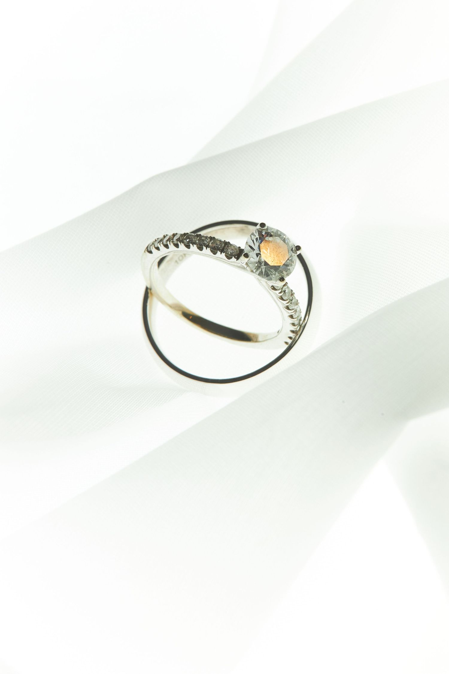 Close-up of delicate diamond engagement ring casting shadows on white surface.