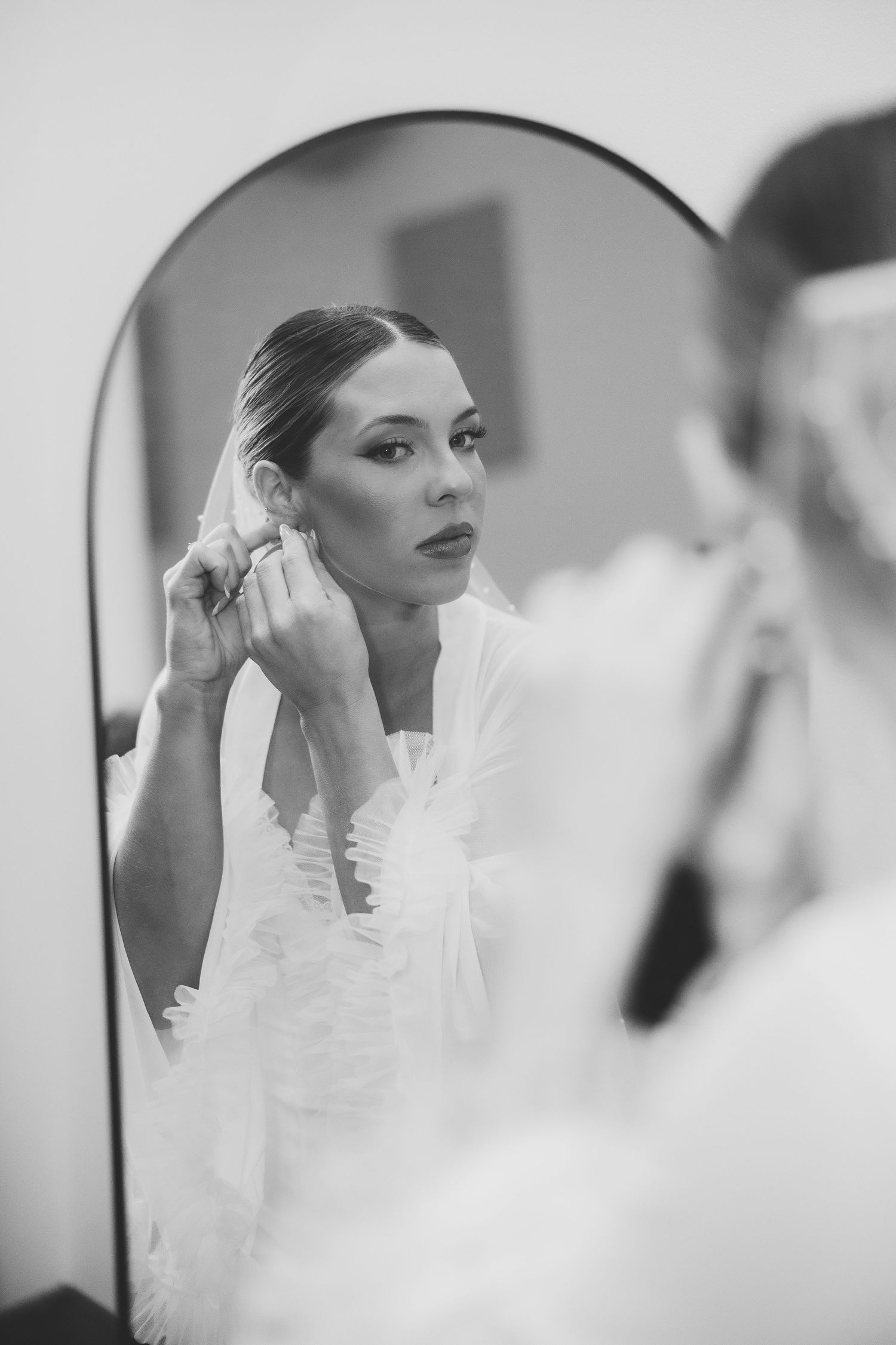 Elegant bride getting ready in white dress reflected in mirror.