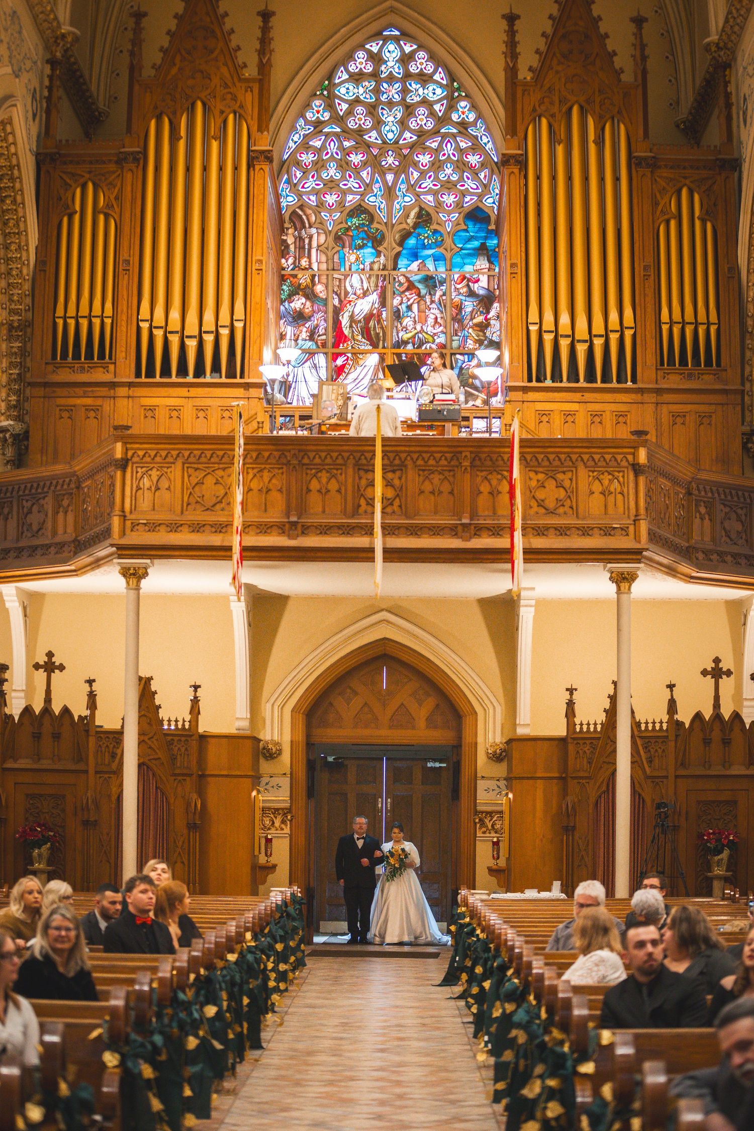 Church interior with golden organ pipes and stained glass windows during wedding ceremony.
