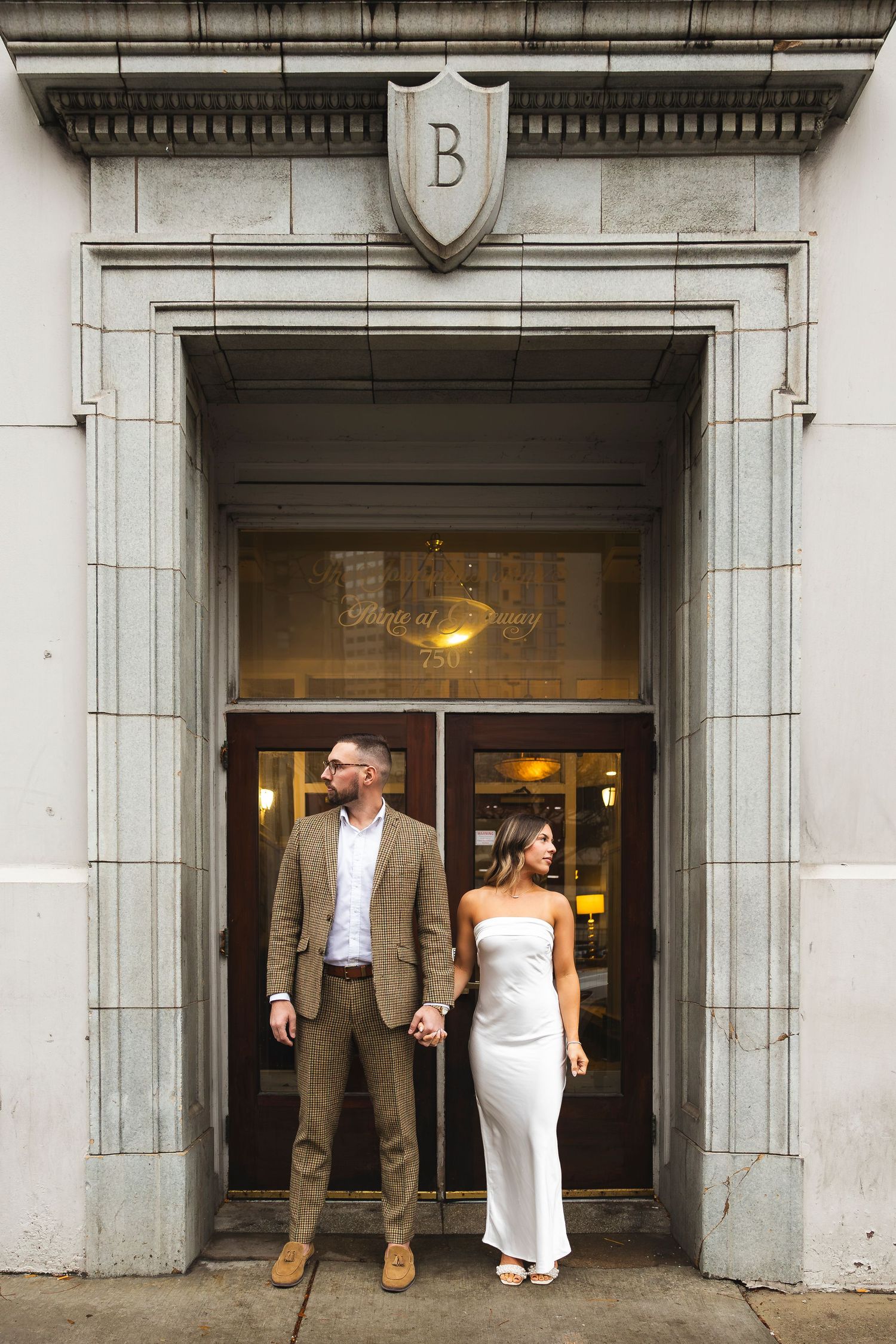 A wedding couple poses in elegant formal attire framed by architectural doorways.