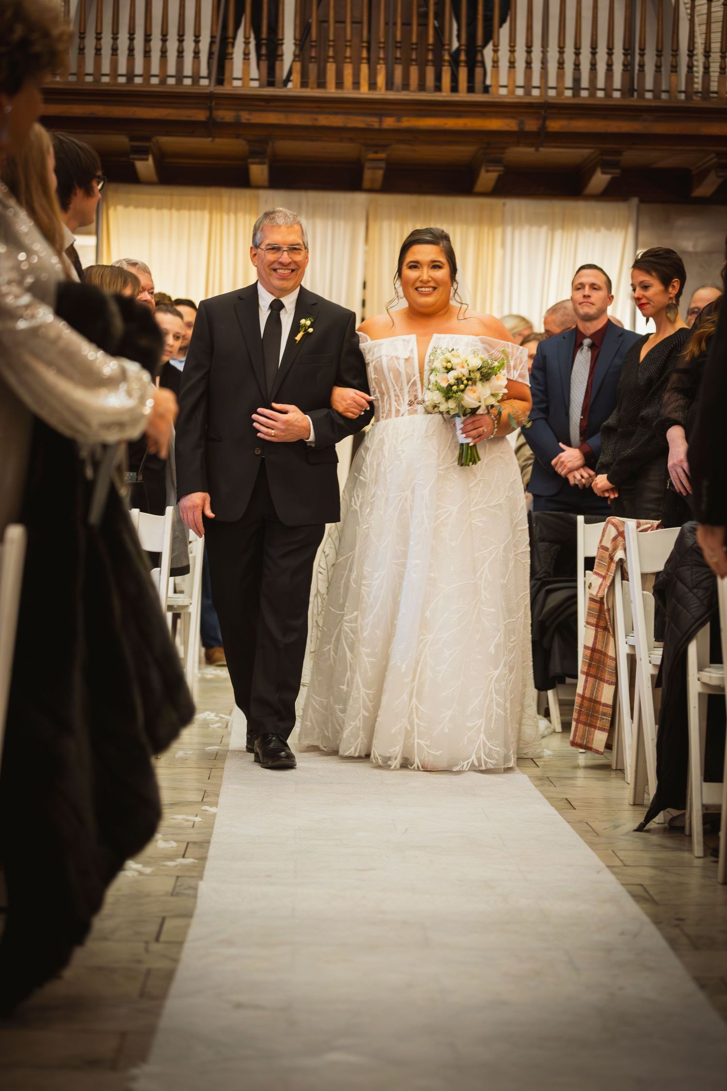 Wedding ceremony processional captured in an elegant venue with stone flooring and wooden details.