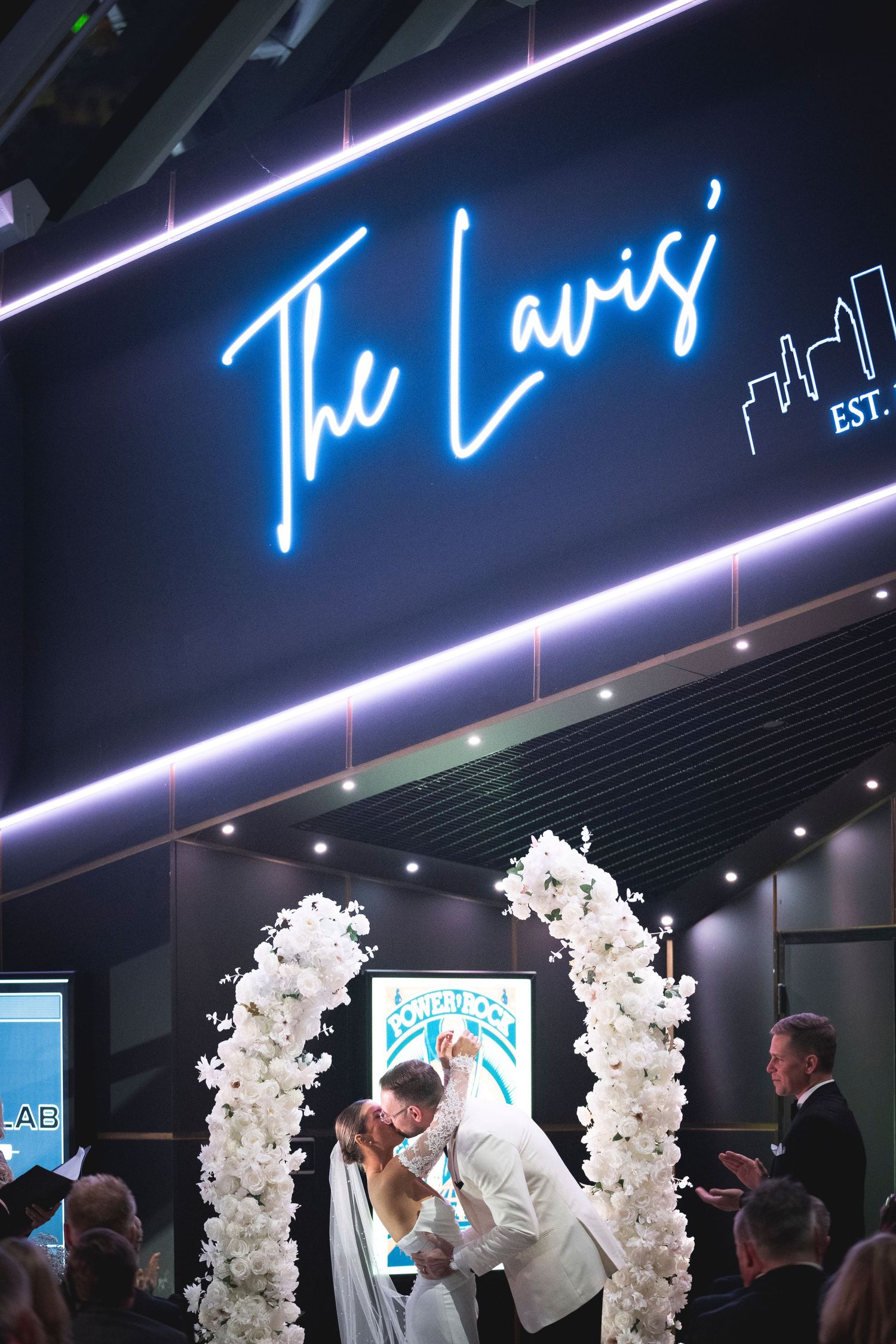 Modern wedding venue with white floral arrangements and blue neon signage.