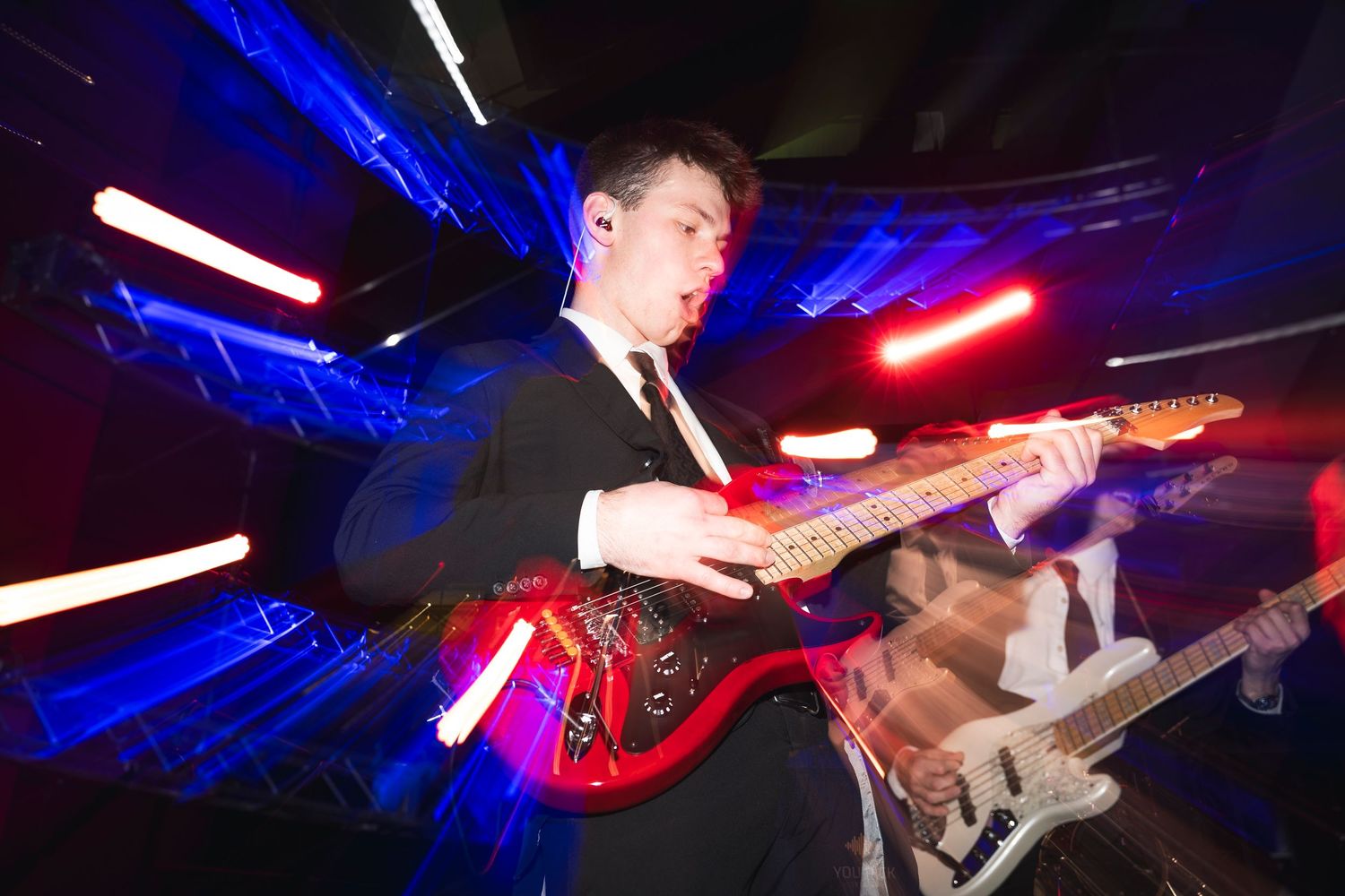Guitarist performs on stage with dramatic blue and red lighting creating an energetic atmosphere.