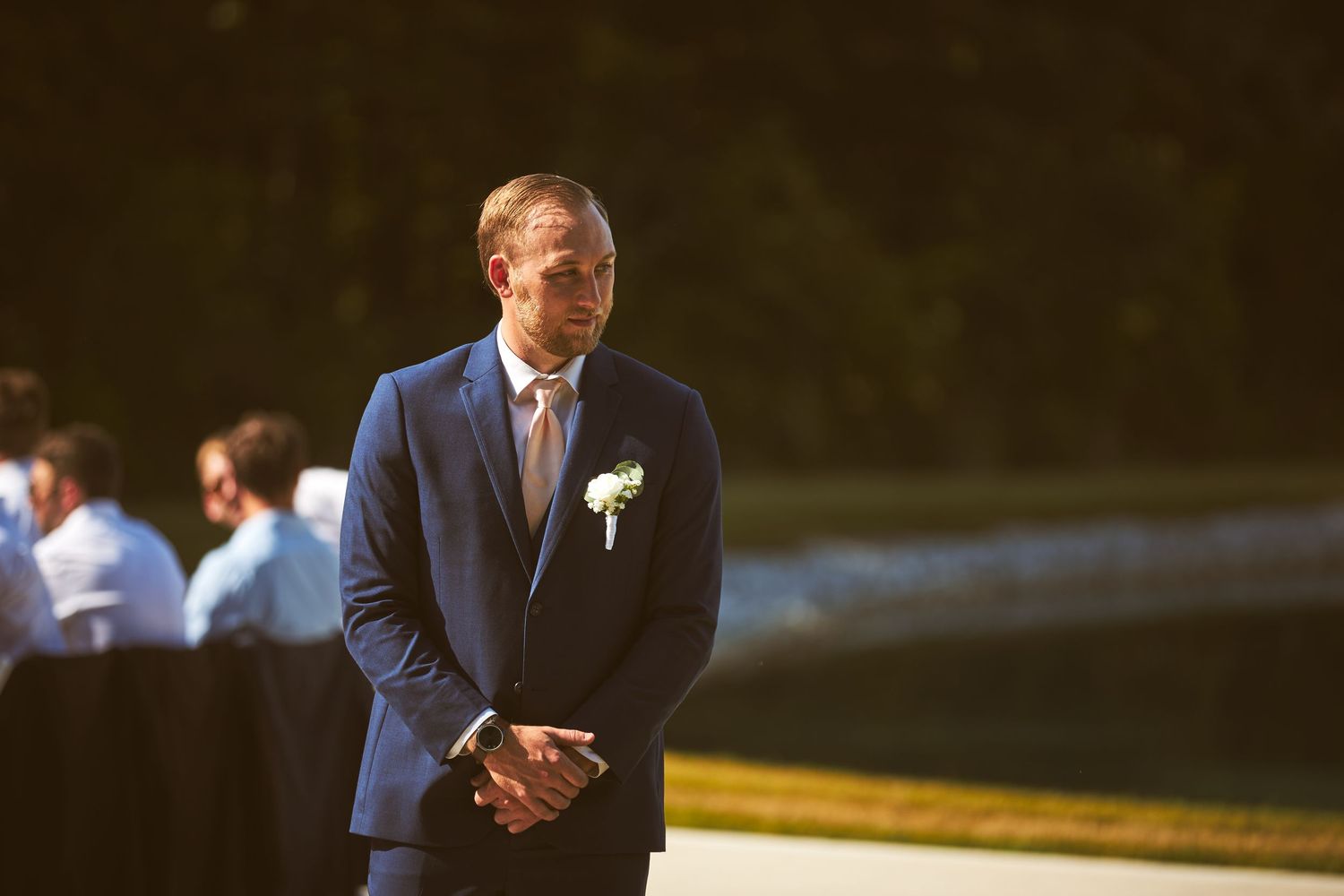 Men in navy suits stand in a row during an outdoor wedding ceremony.