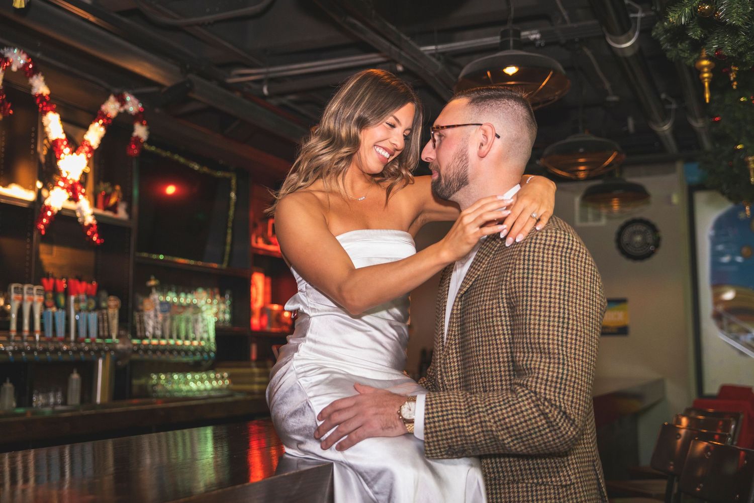 Couple sharing laughs and drinks at a festively decorated bar with ambient lighting.