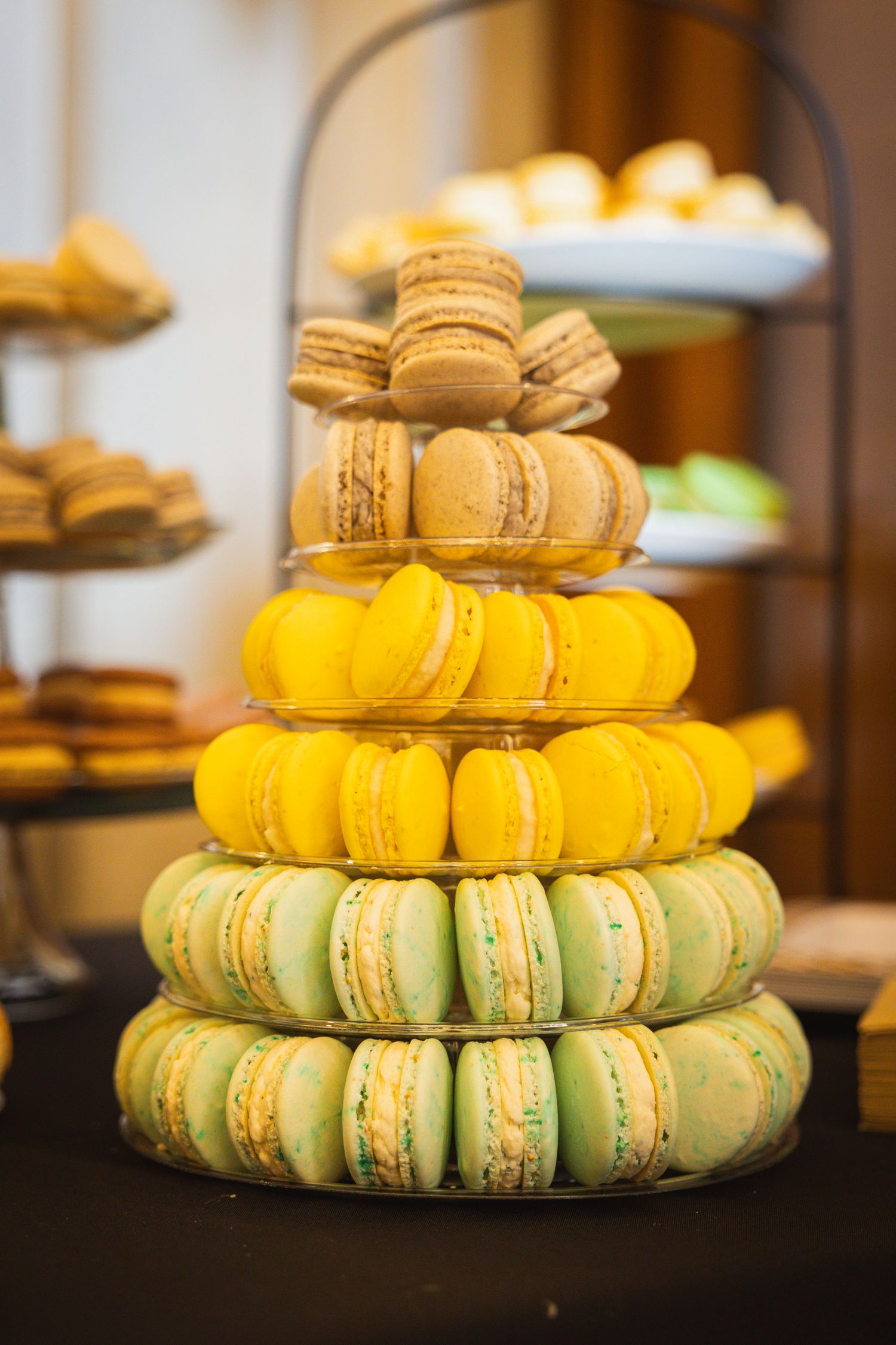 Tiered display of yellow and mint green macarons arranged in an elegant wedding dessert presentation.