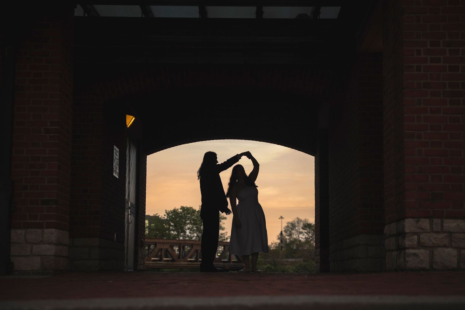 A silhouetted couple dances beneath an archway during golden hour.