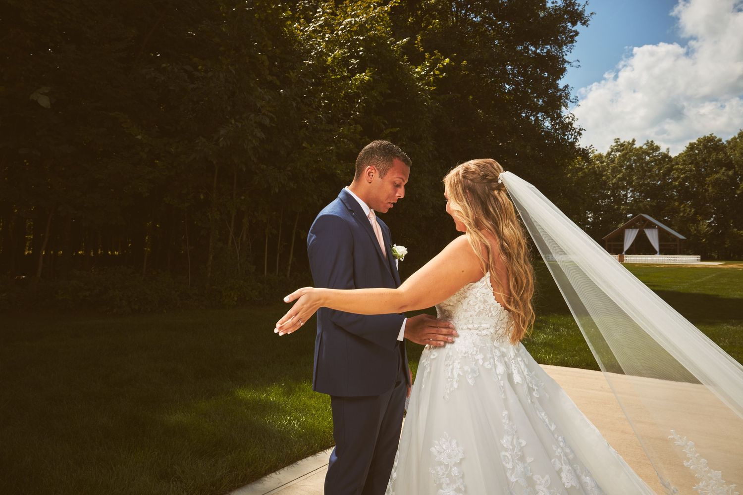 Wedding couple posing outdoors on a sunny day with white clouds.