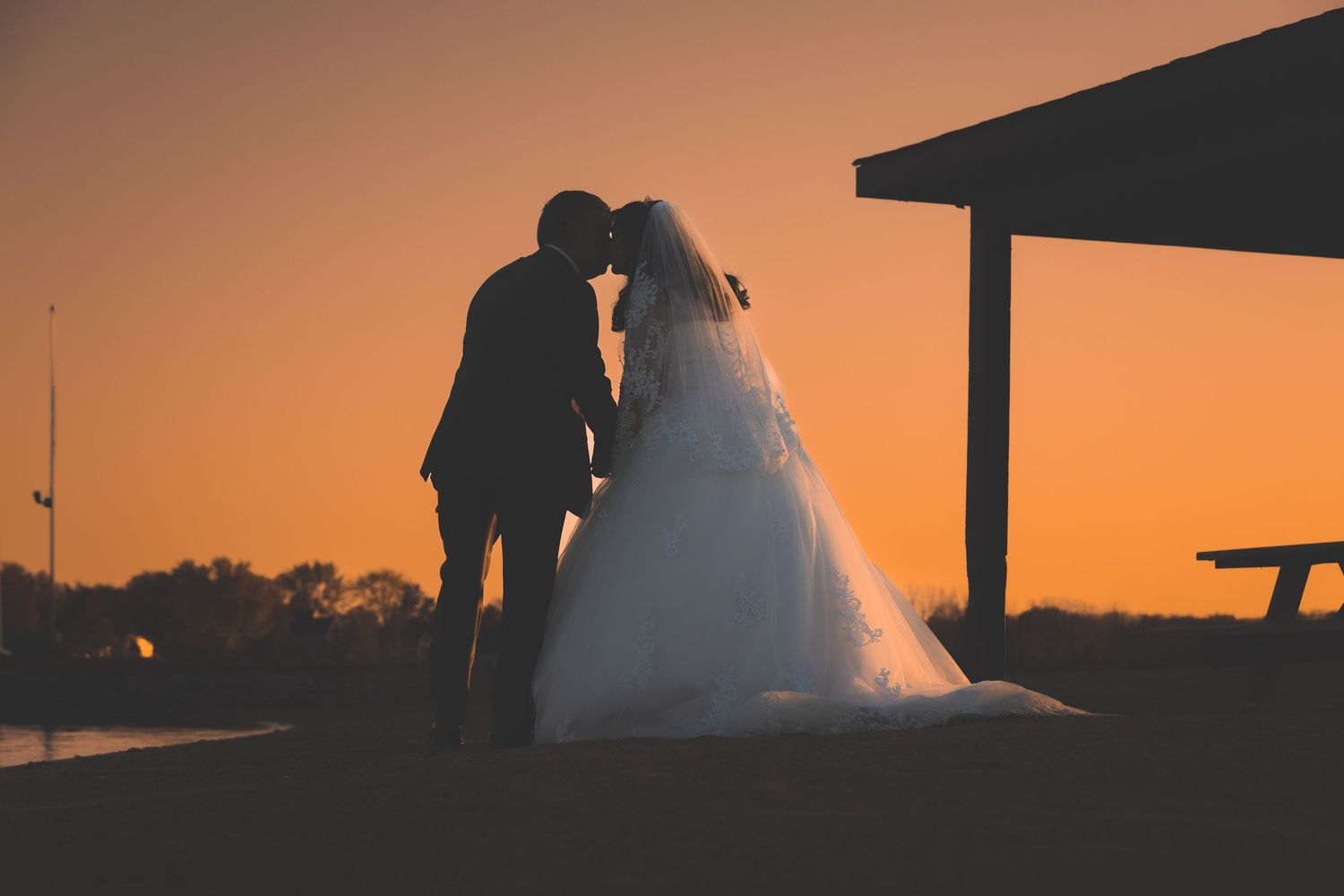 Silhouettes against a vibrant orange sunset sky create a romantic coastal wedding scene.
