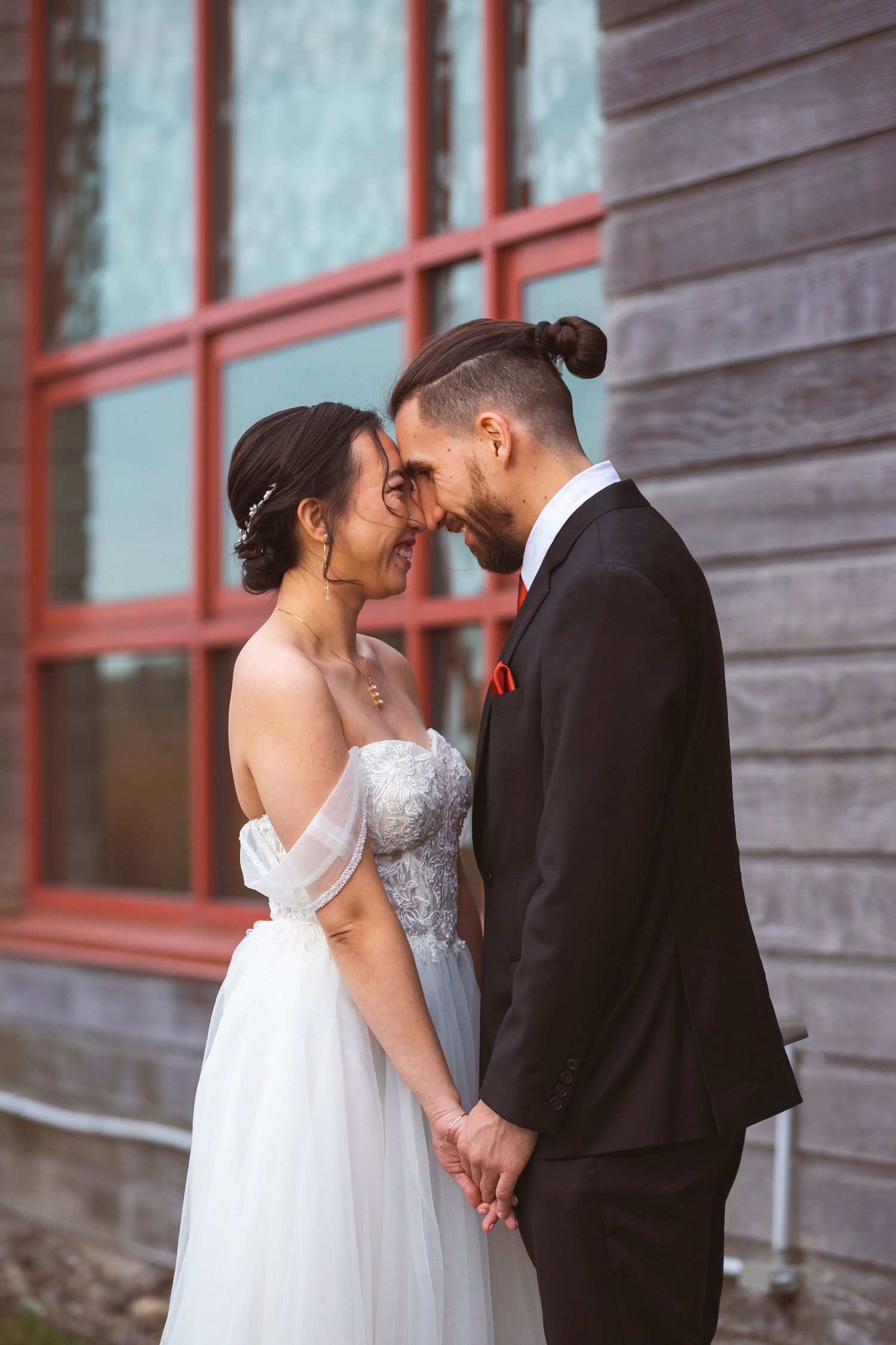 Intimate wedding portrait against rustic wooden walls with red window frames.