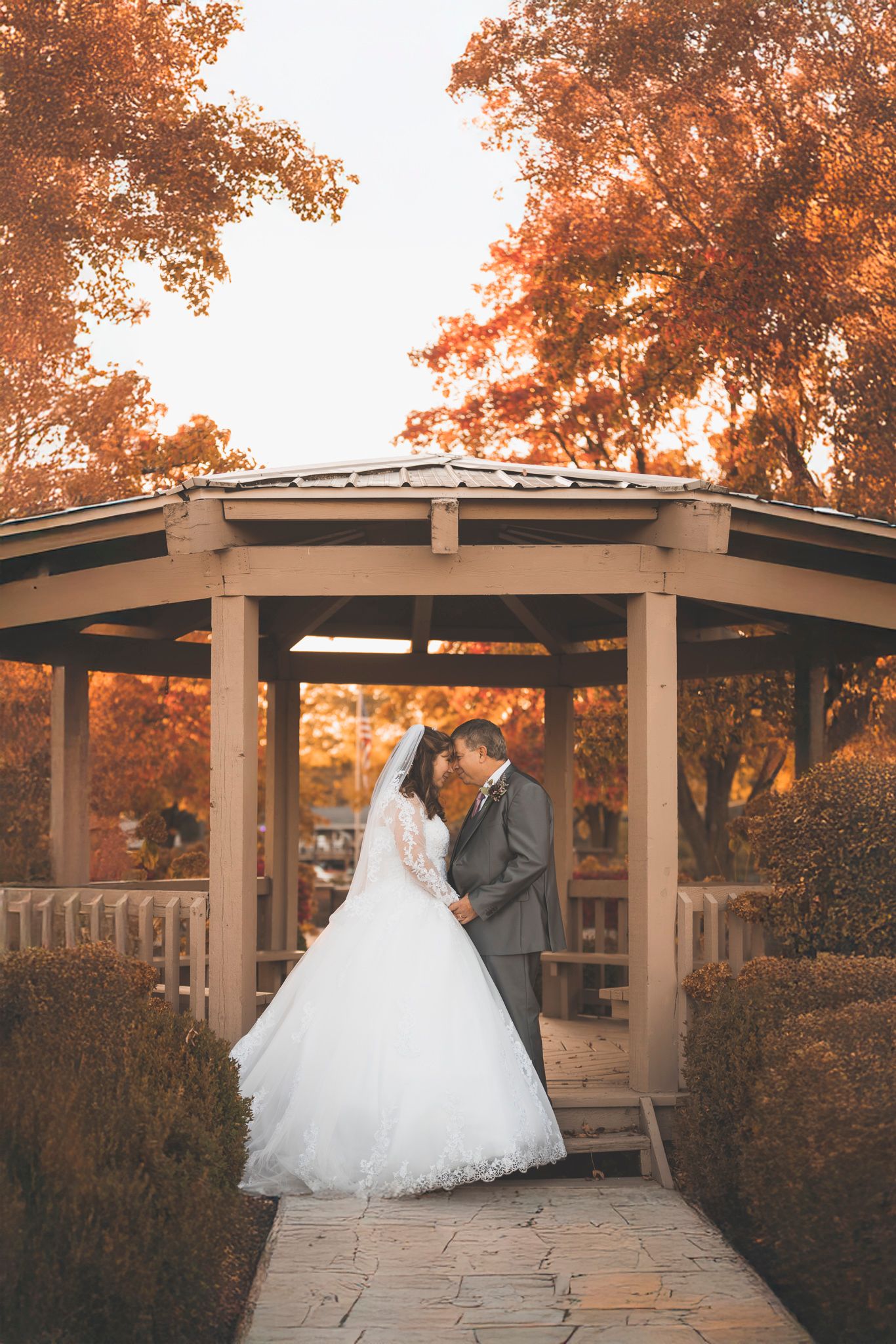A romantic moment captured under a curved pergola with autumn foliage overhead.