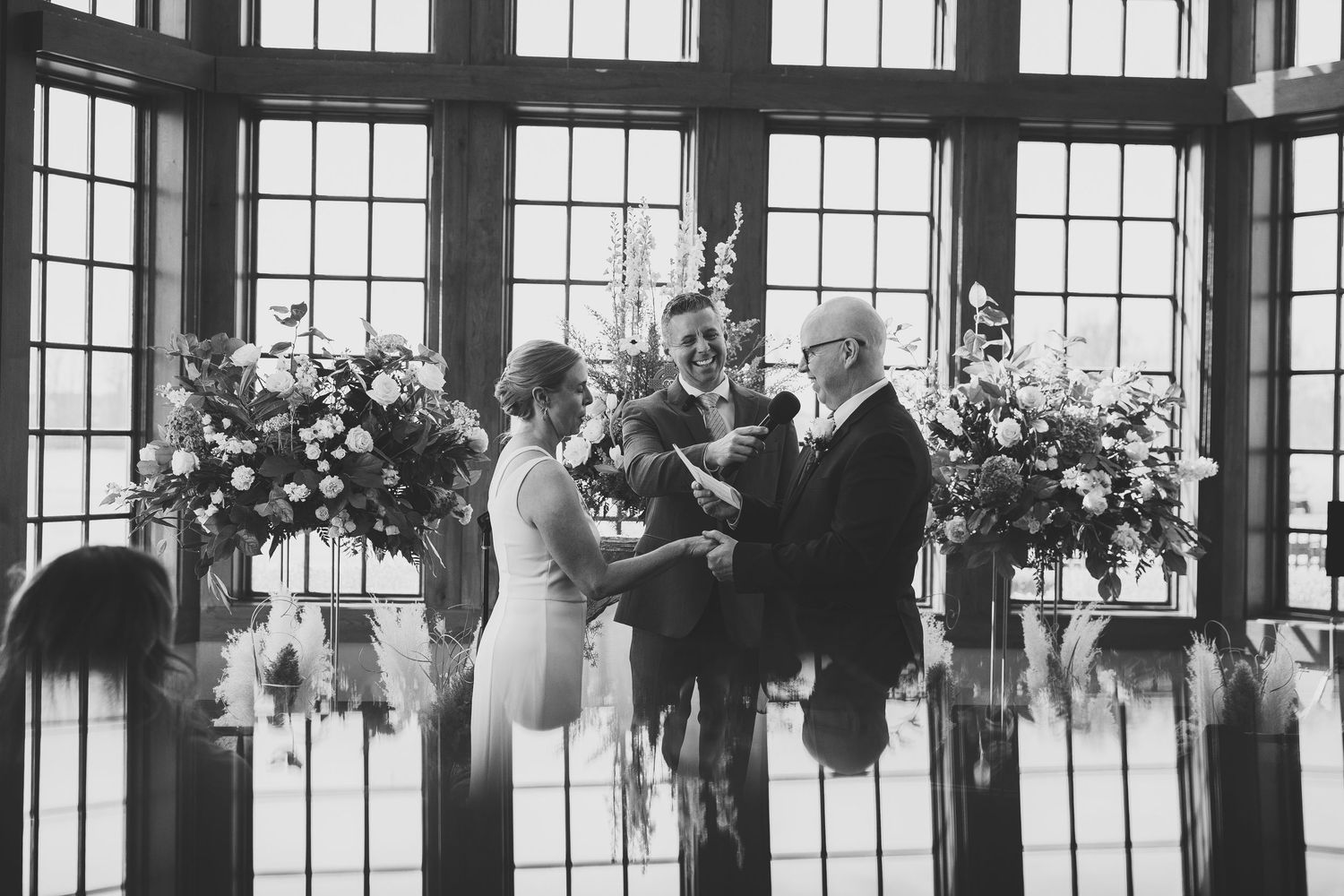 Indoor wedding ceremony setup with large windows and hanging floral arrangements.