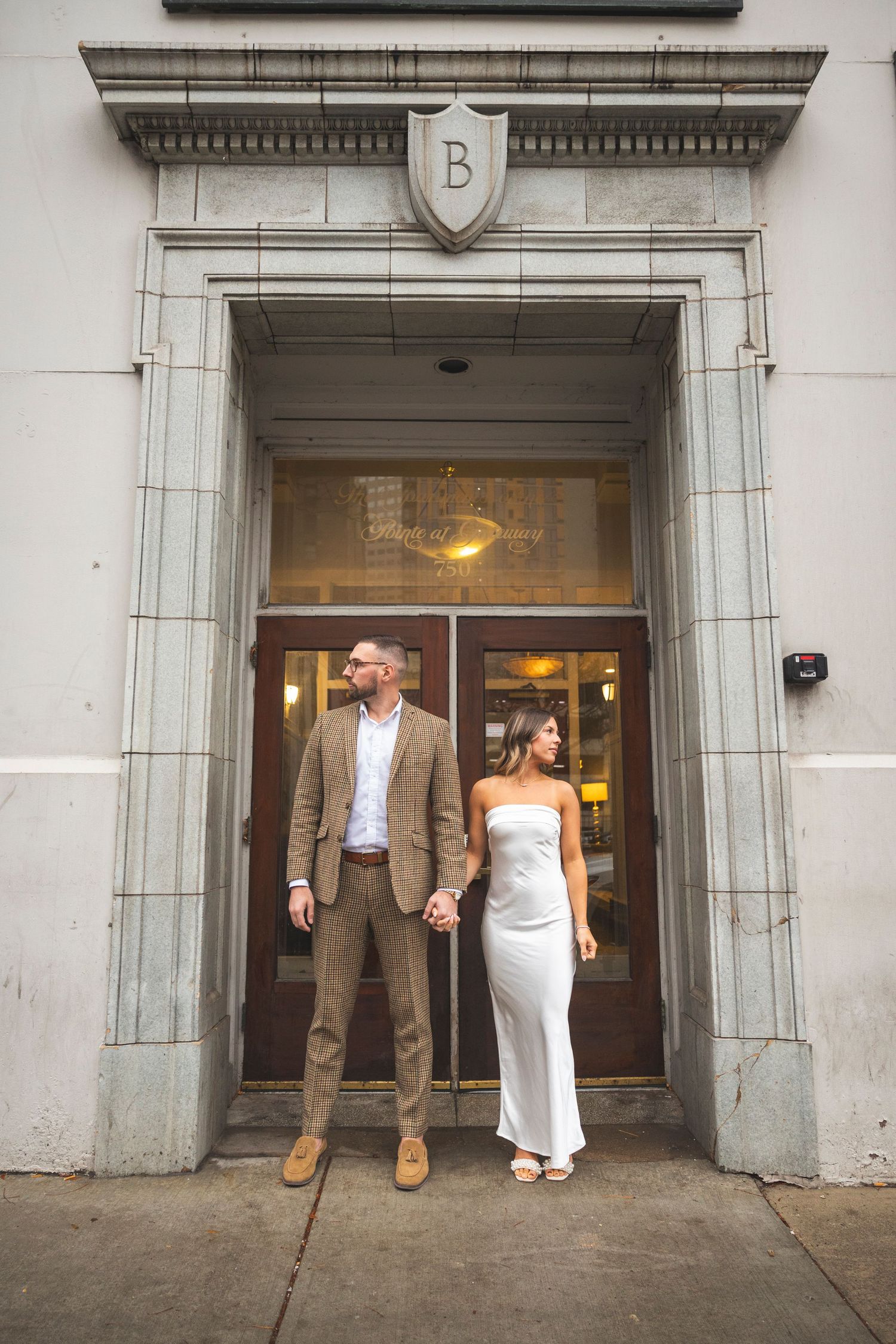 Elegant couple stands in front of a stone archway entrance in formal attire.