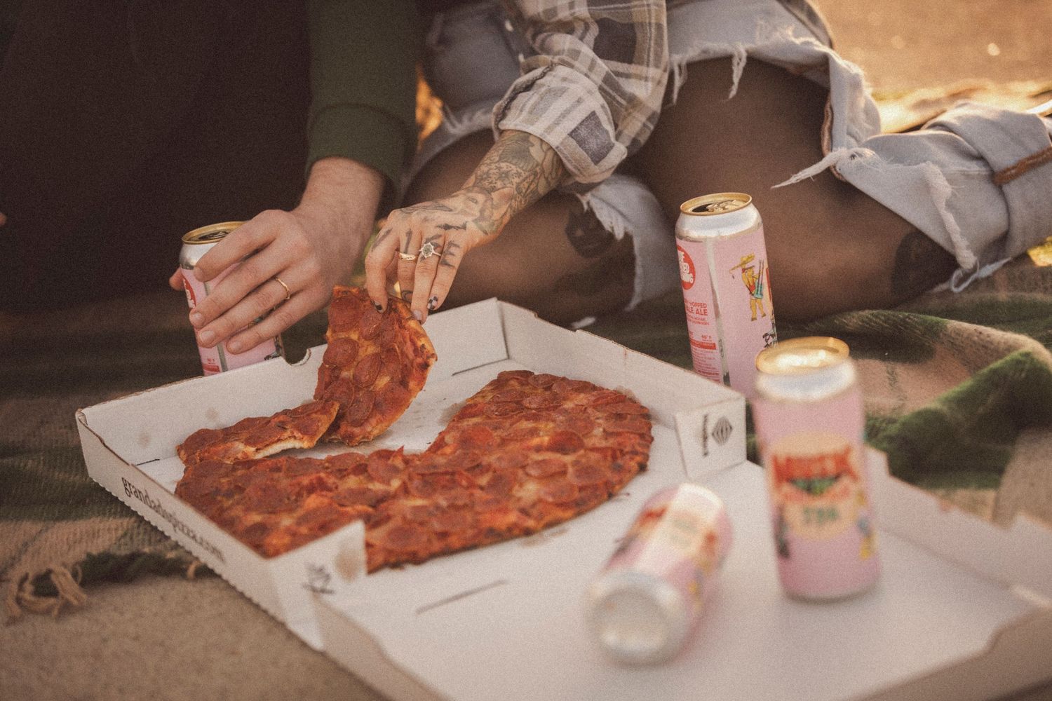 Close-up of hands sharing pizza and drinks during an outdoor date.