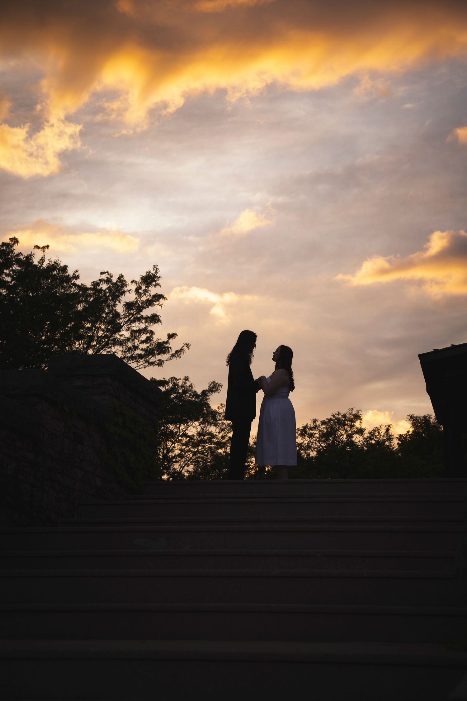 Silhouettes of two people against a dramatic sunset sky with clouds.