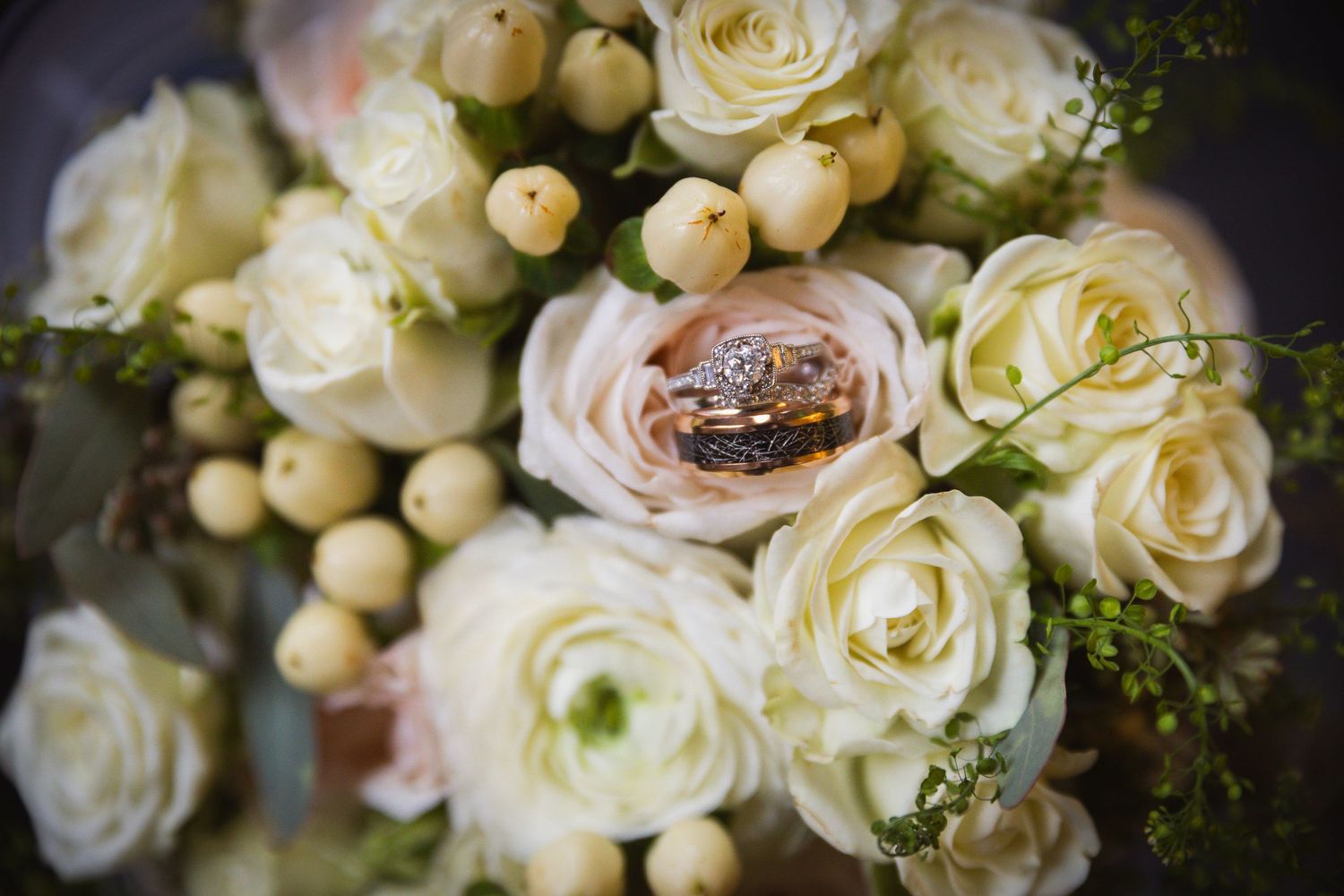 Elegant cream and white roses arranged in a romantic wedding bouquet with delicate berries.