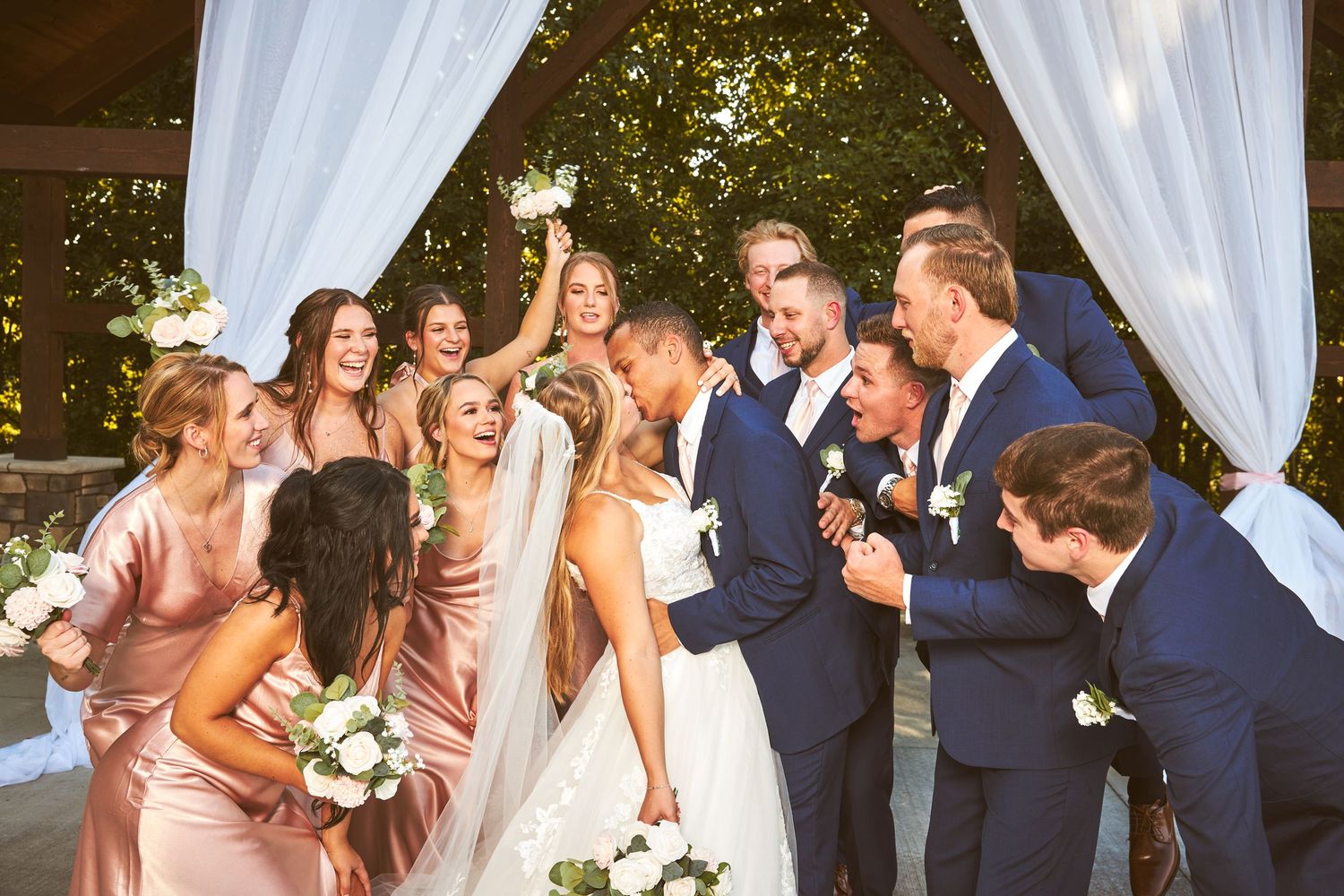 Wedding party members celebrate under a draped outdoor pavilion.