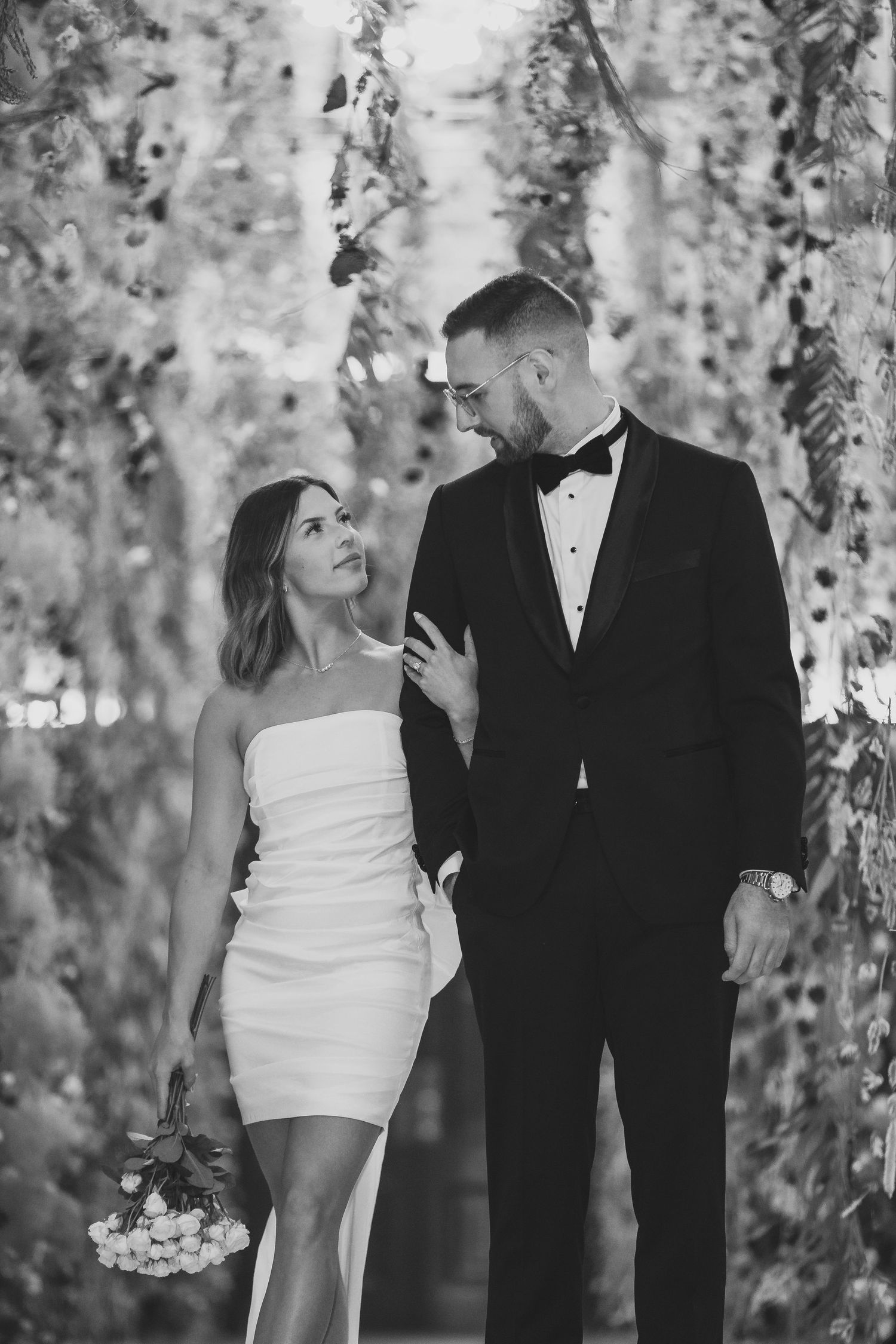 A black and white photo of a couple sharing an intimate moment beneath hanging decor.