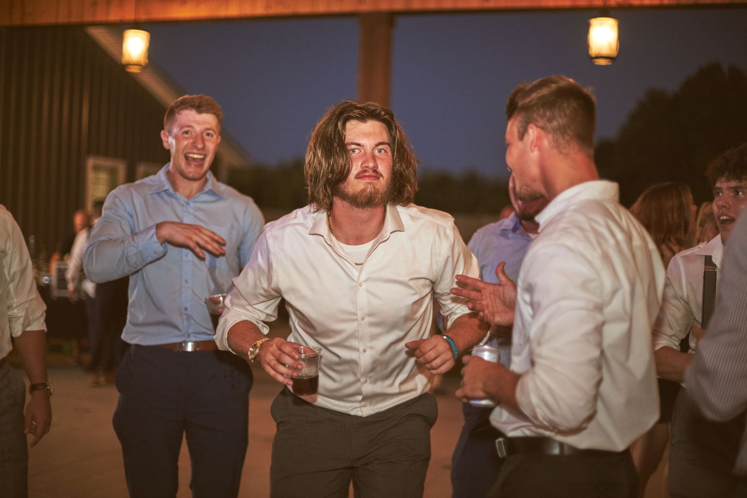 Energetic guests dance and celebrate at a lively wedding reception party during sunset.