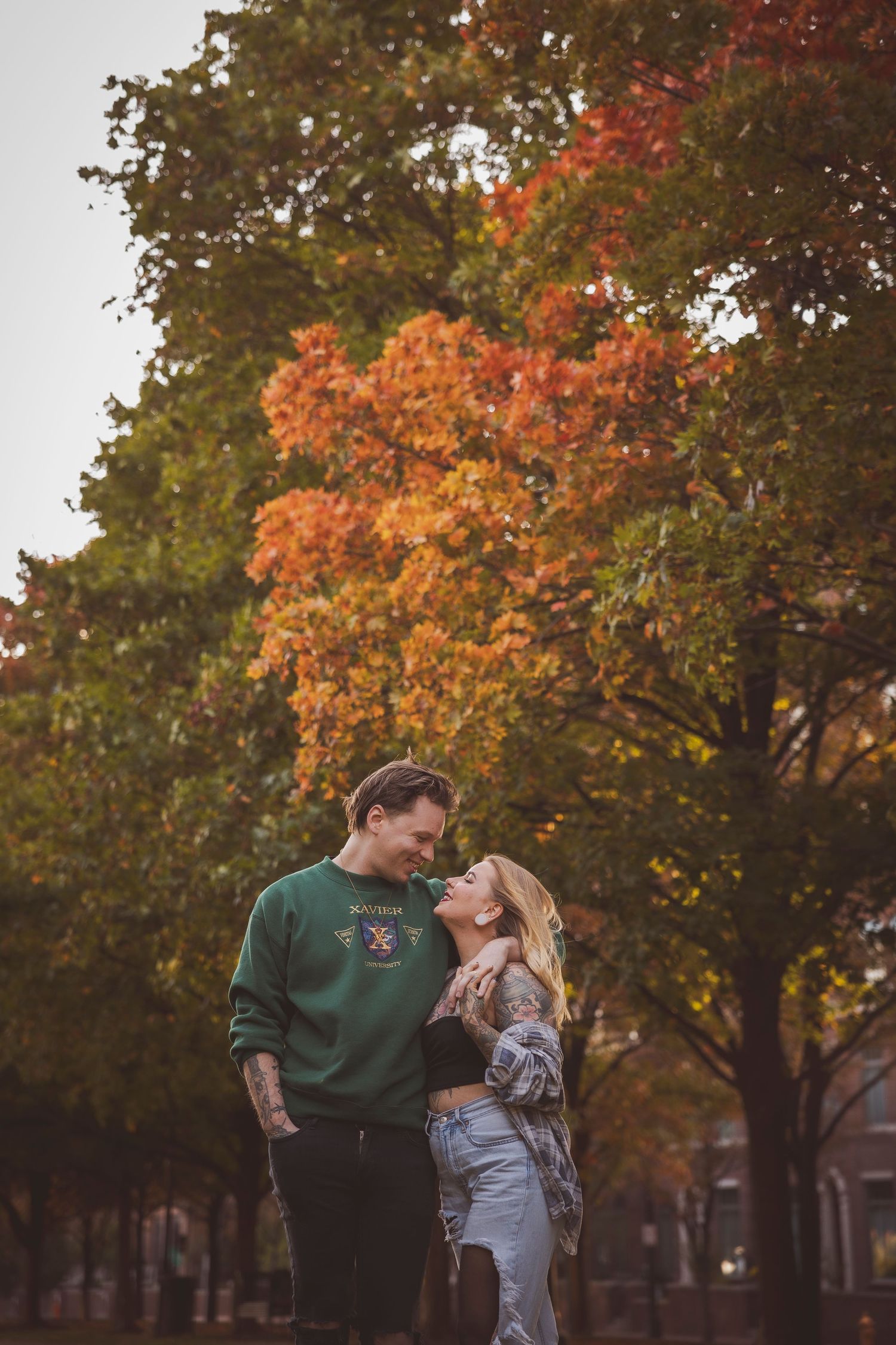 Couple embraces under vibrant autumn trees with red and orange foliage.