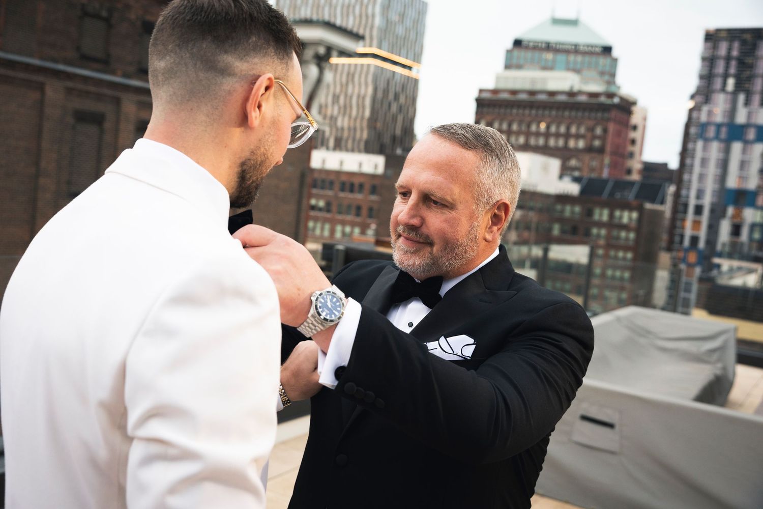 People in formal black attire greet each other warmly on a city rooftop.