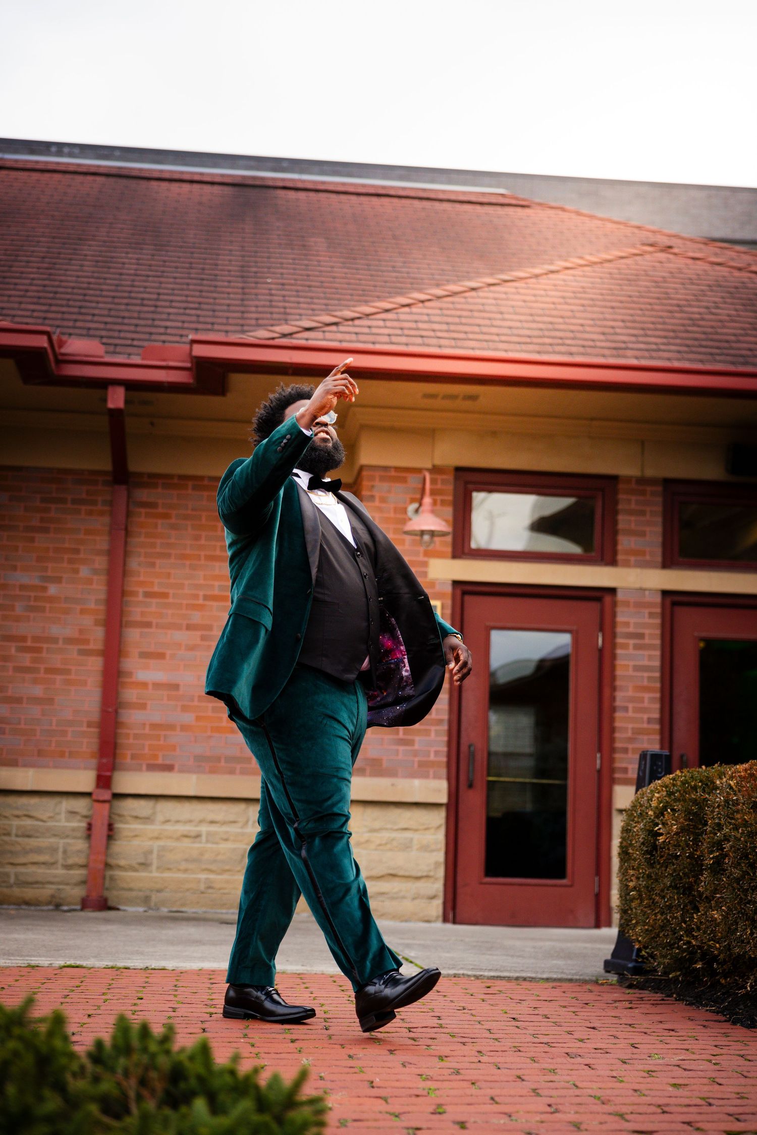 Energetic dance movements photographed in sequence showing emerald green suit against red brick architecture.